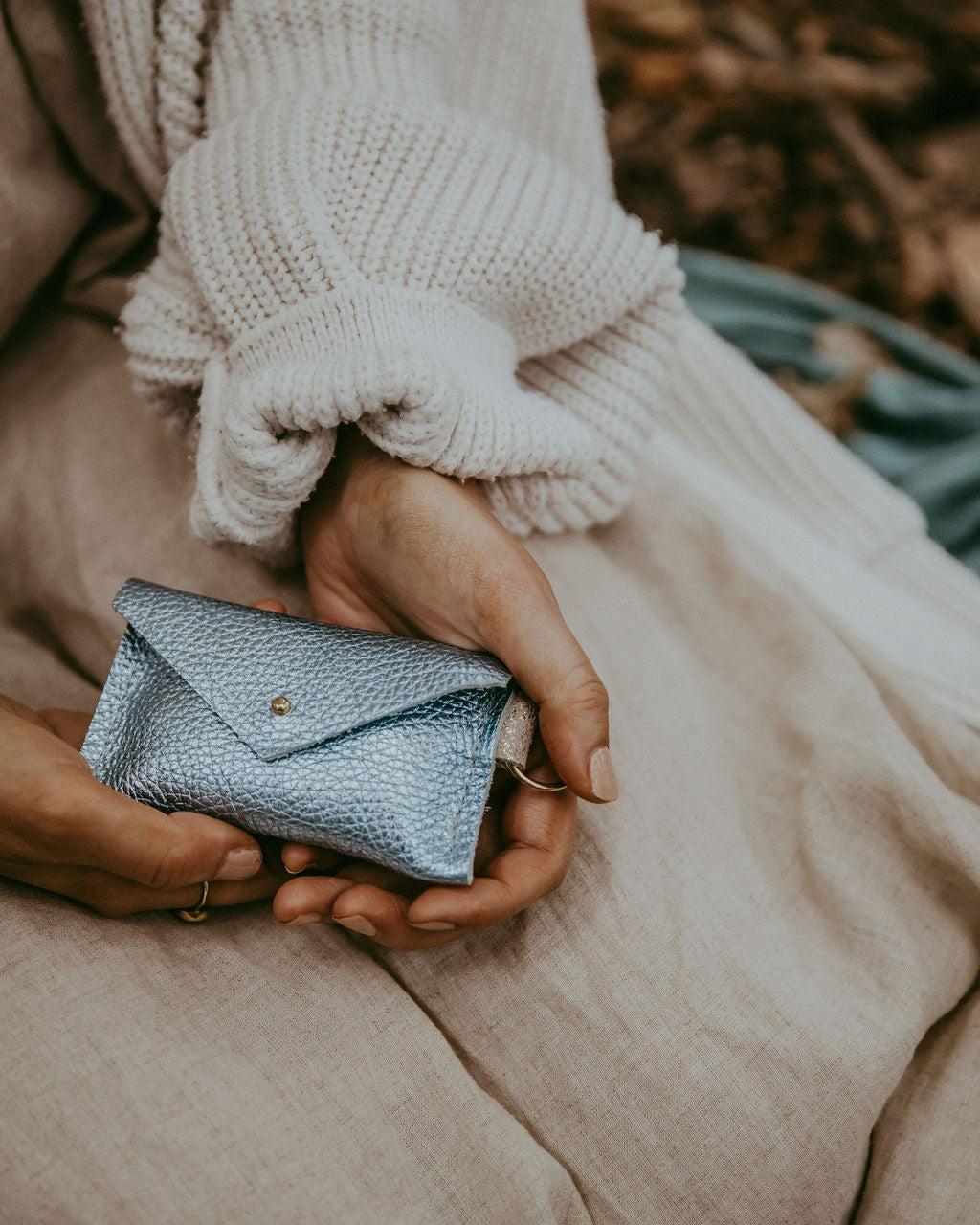 Person holding a small blue wallet with a blurred natural background