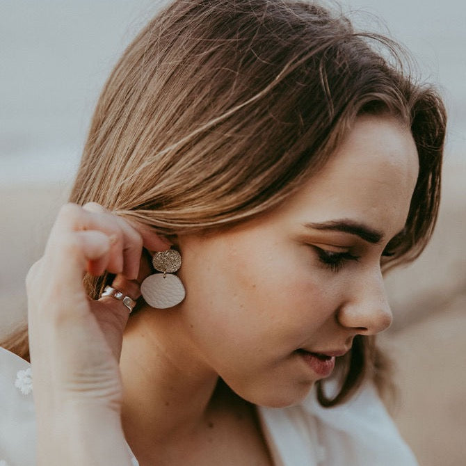 Bride wears gold sparkly cream statement pebble blob earrings.