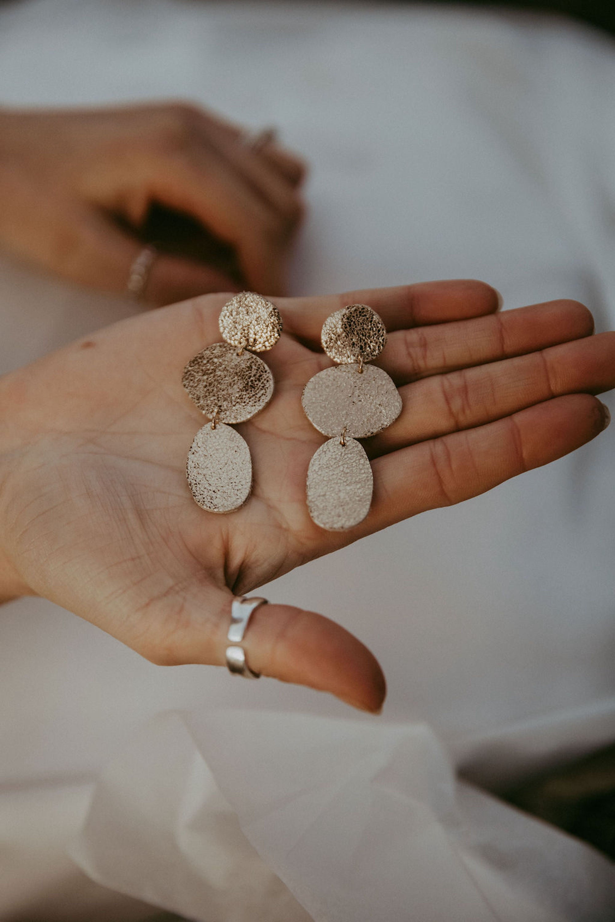 Gold statement earrings held in brides hand.