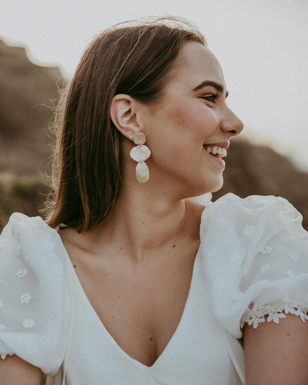 Bride wears gold statement leather earrings, a trio of gold pebble shapes.