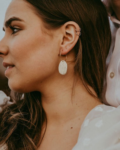 Couple on their wedding day, bride has brown hair and is wearing gold hoop earrings with a statement leather gold pebble detail.