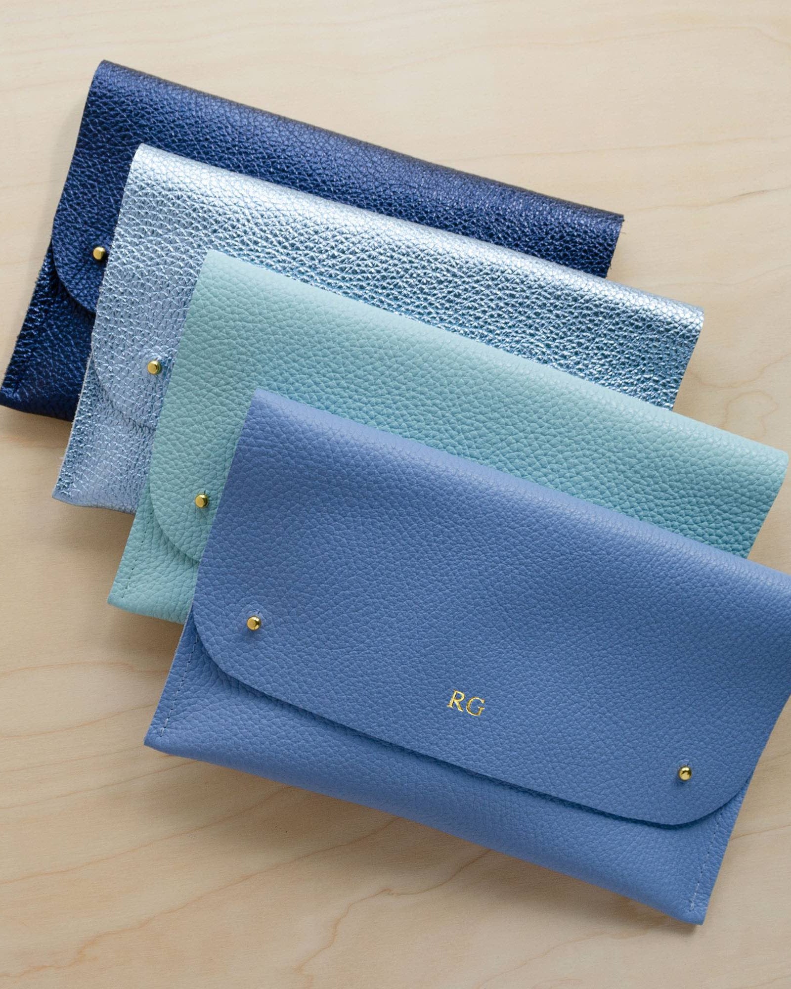 Four leather clutch bags in various blue shades, the first has RG initials stamped.