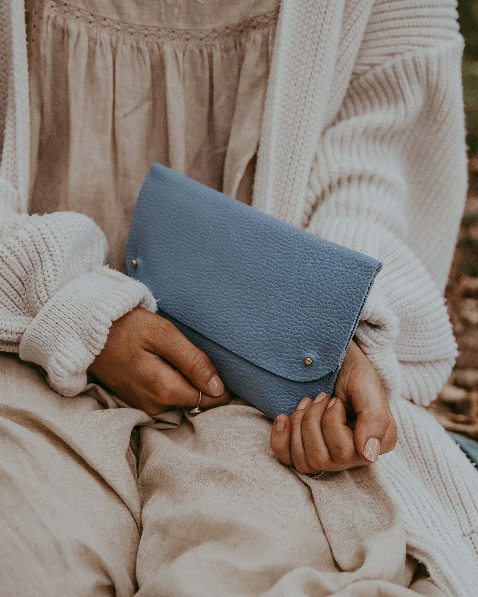 Woman holding the leather clutch bag in powder blue.