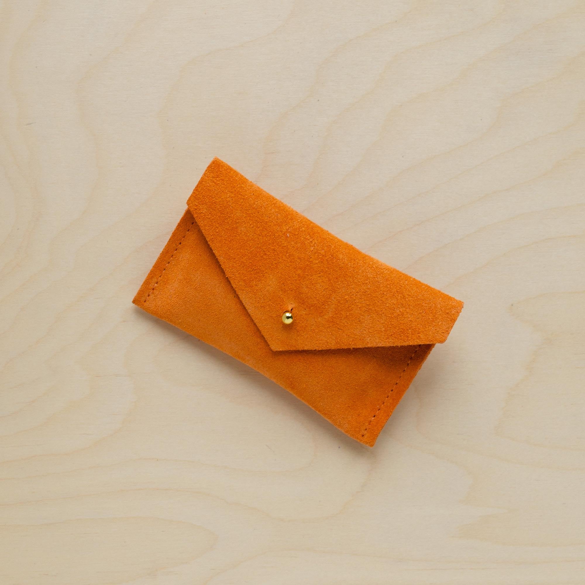 A suede Small Notions Pouch in orange. Complete with a stud for secure closing.