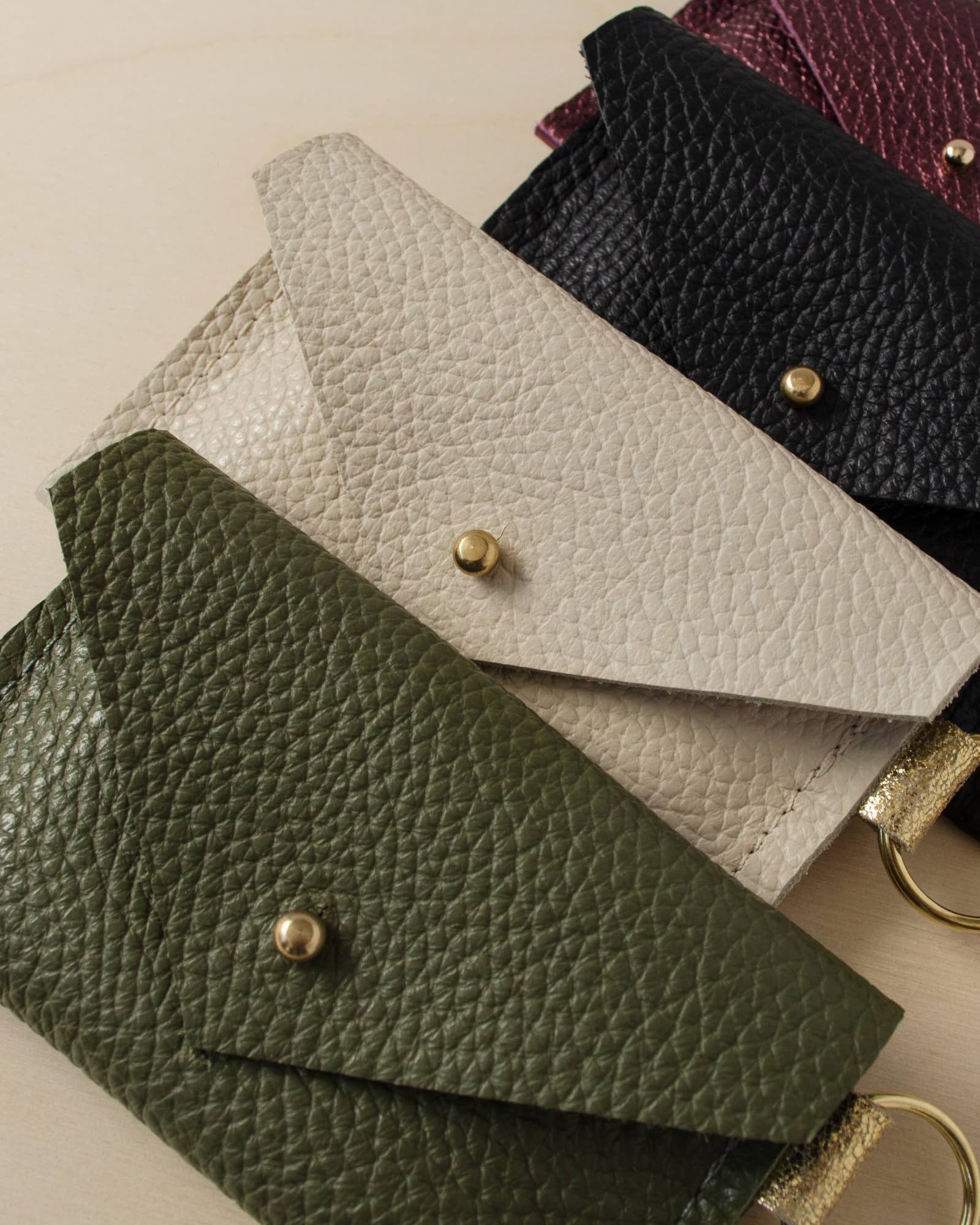 Four leather keyring card holders in, Metallic Berry, Black, Cream and Olive Green.