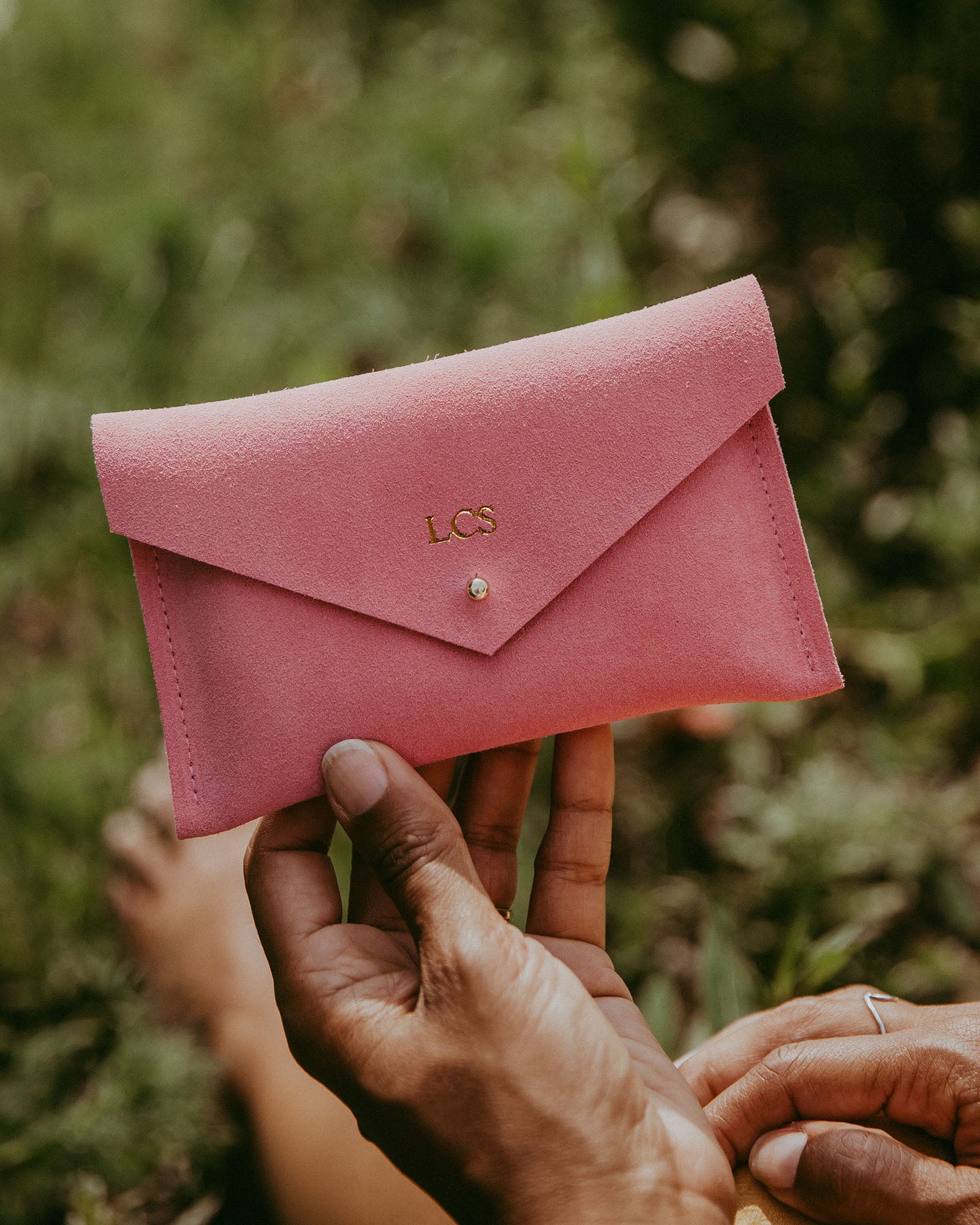 Coral pink suede purse with envelope style is held by a woman in summer. The design of the purse features a minimalist envelope style.