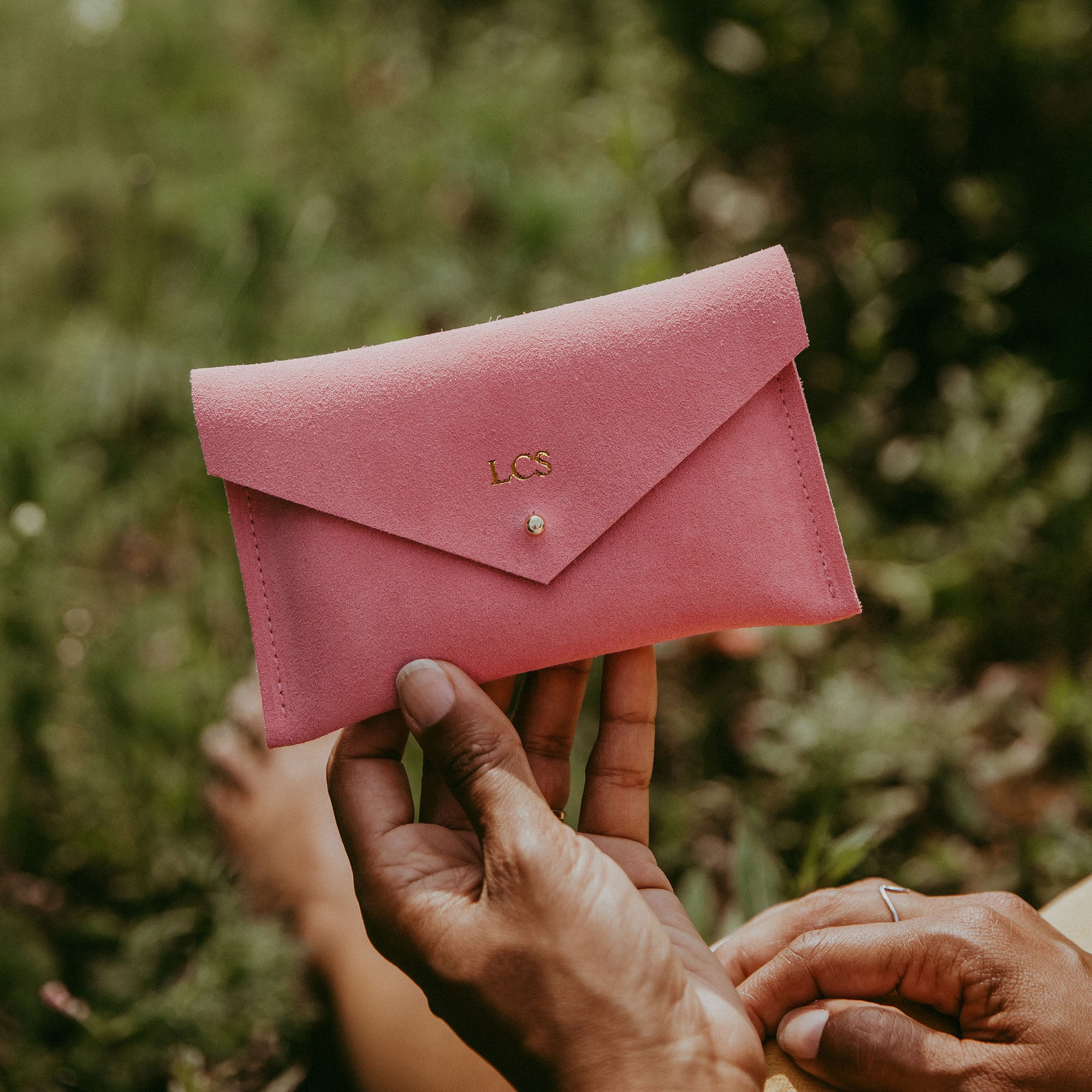 Coral pink suede purse with envelope style is held by a woman in summer. The design of the purse features a minimalist envelope style.
