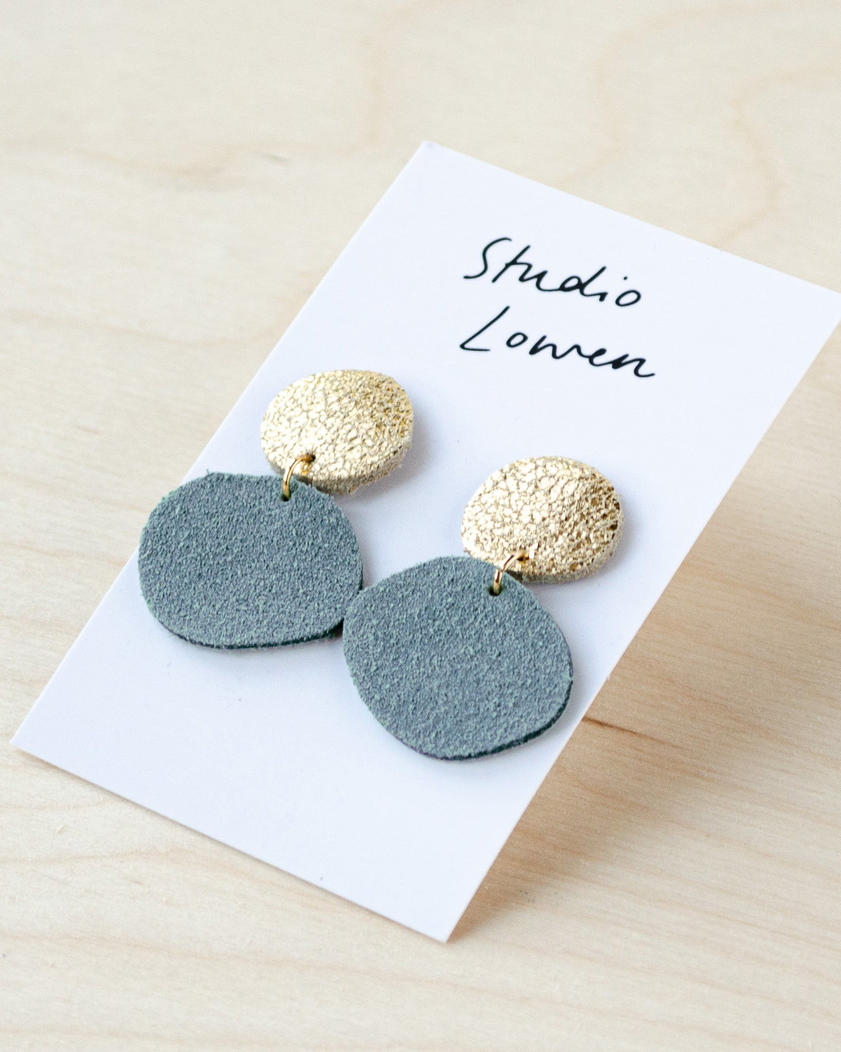 Bili Pop leather and suede earrings featuring a small circle at the top in gold and a larger drop circle at the bottom in pale blue.