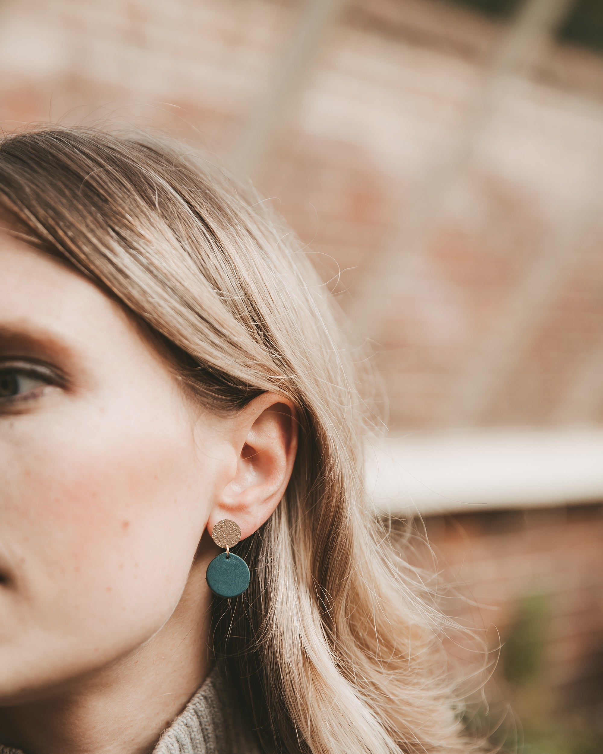 Close-up of a person wearing a green  and gold leather earring with a blurred background.