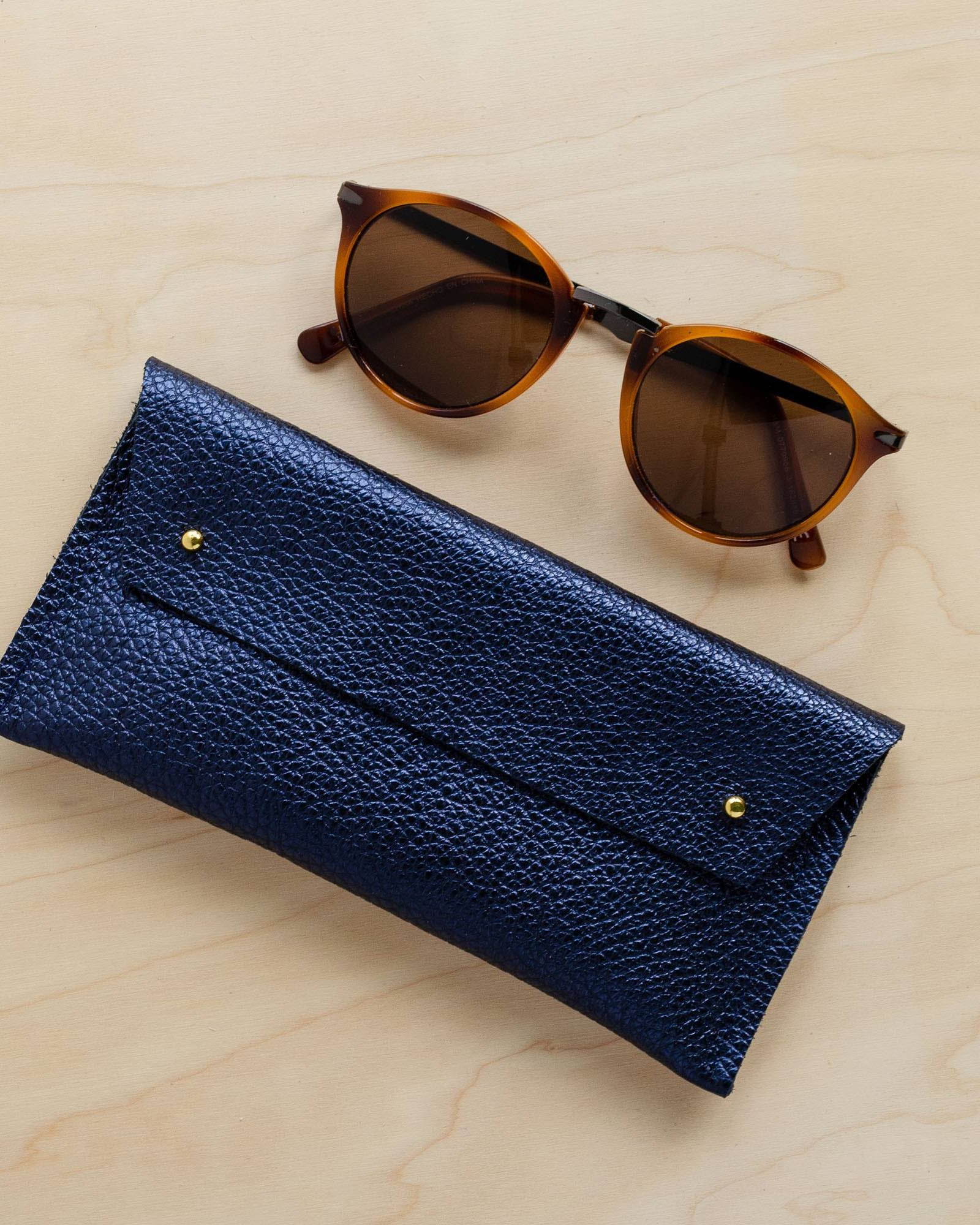 Metallic Navy leather double stud glasses case with sunglasses.
