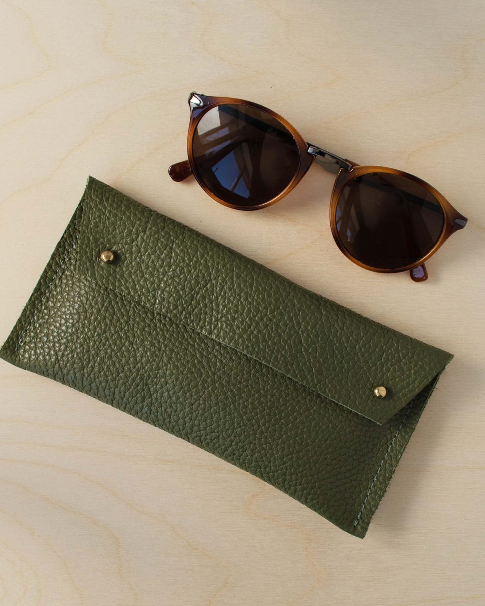 Olive green leather glasses case on a wooden background.