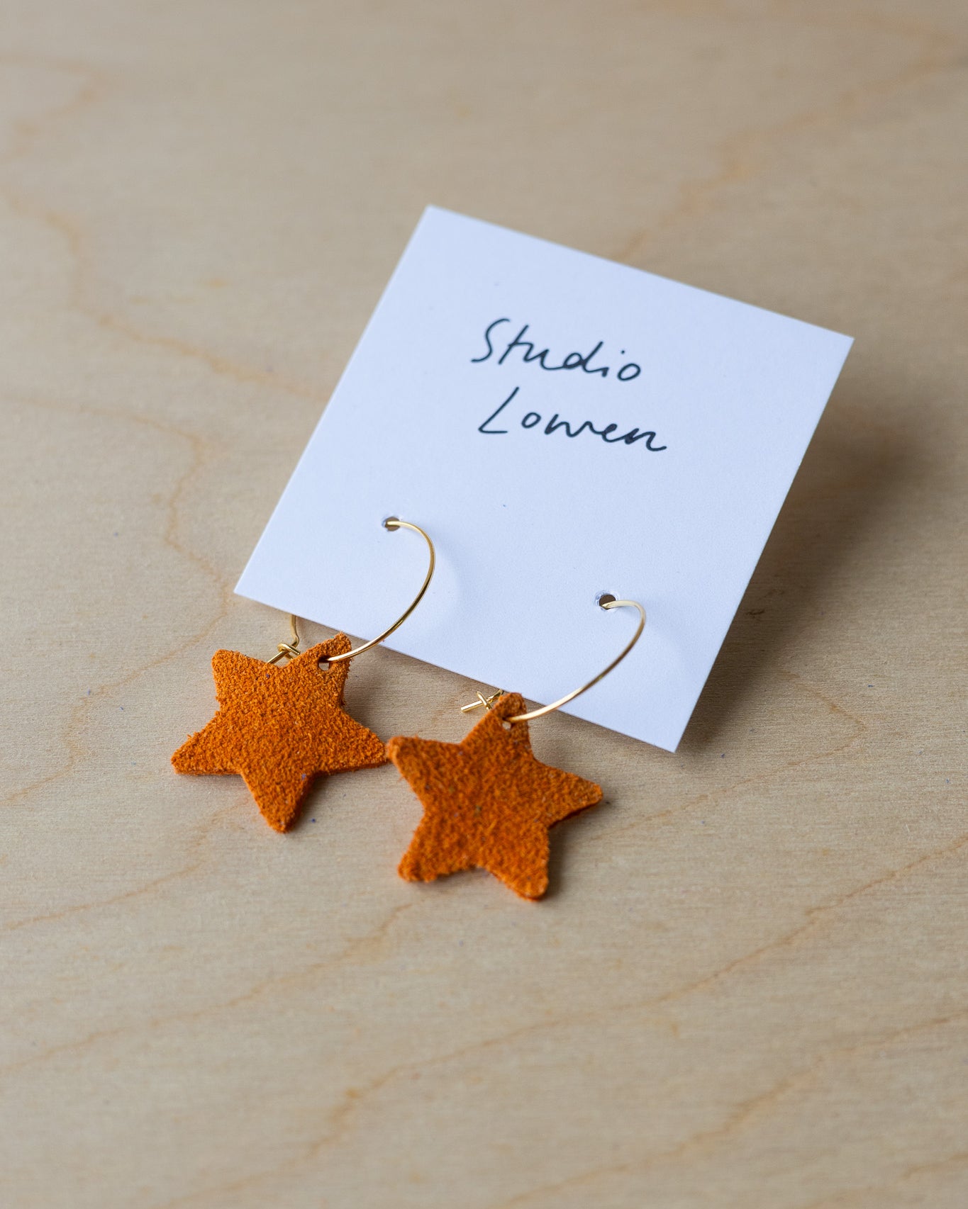 Star-shaped earrings on a card with 'Studio Lowen' text, placed on a wooden surface.