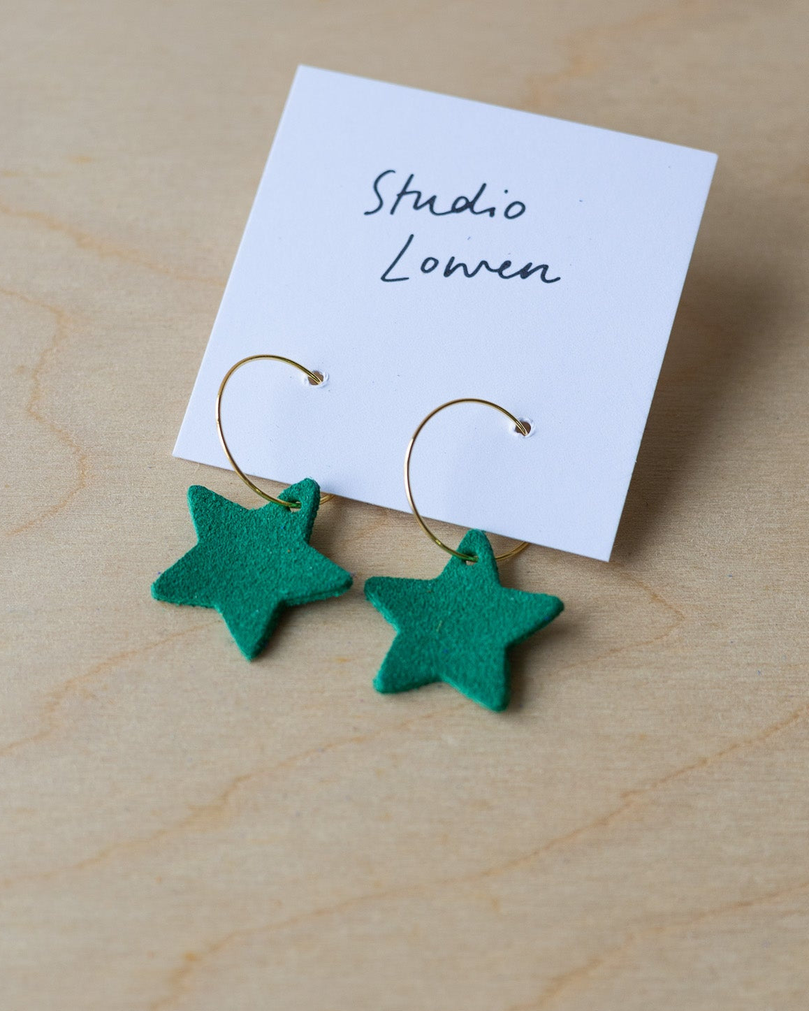 Green star-shaped earrings on a card with 'Studio Lowen' text, placed on a wooden surface.
