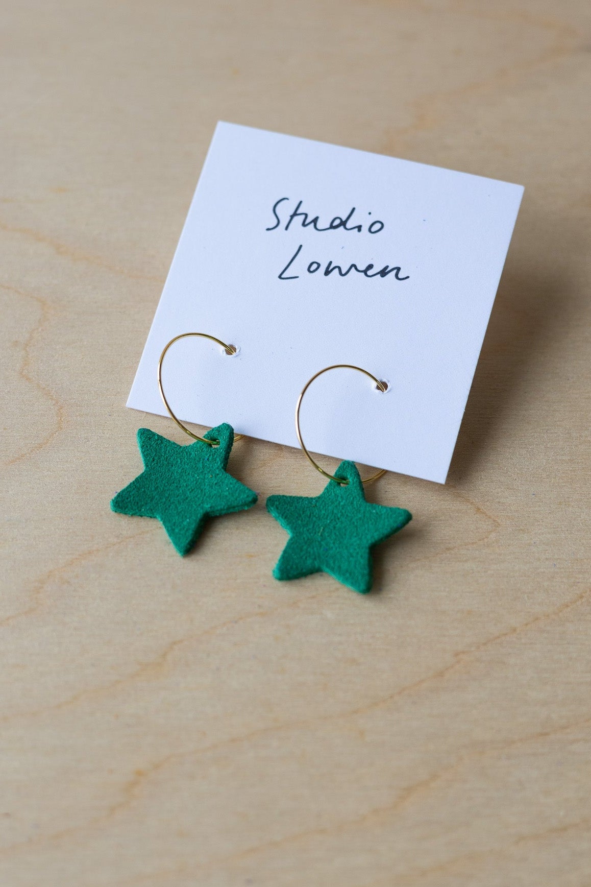 Green star-shaped earrings on a card with 'Studio Lowen' text, placed on a wooden surface.