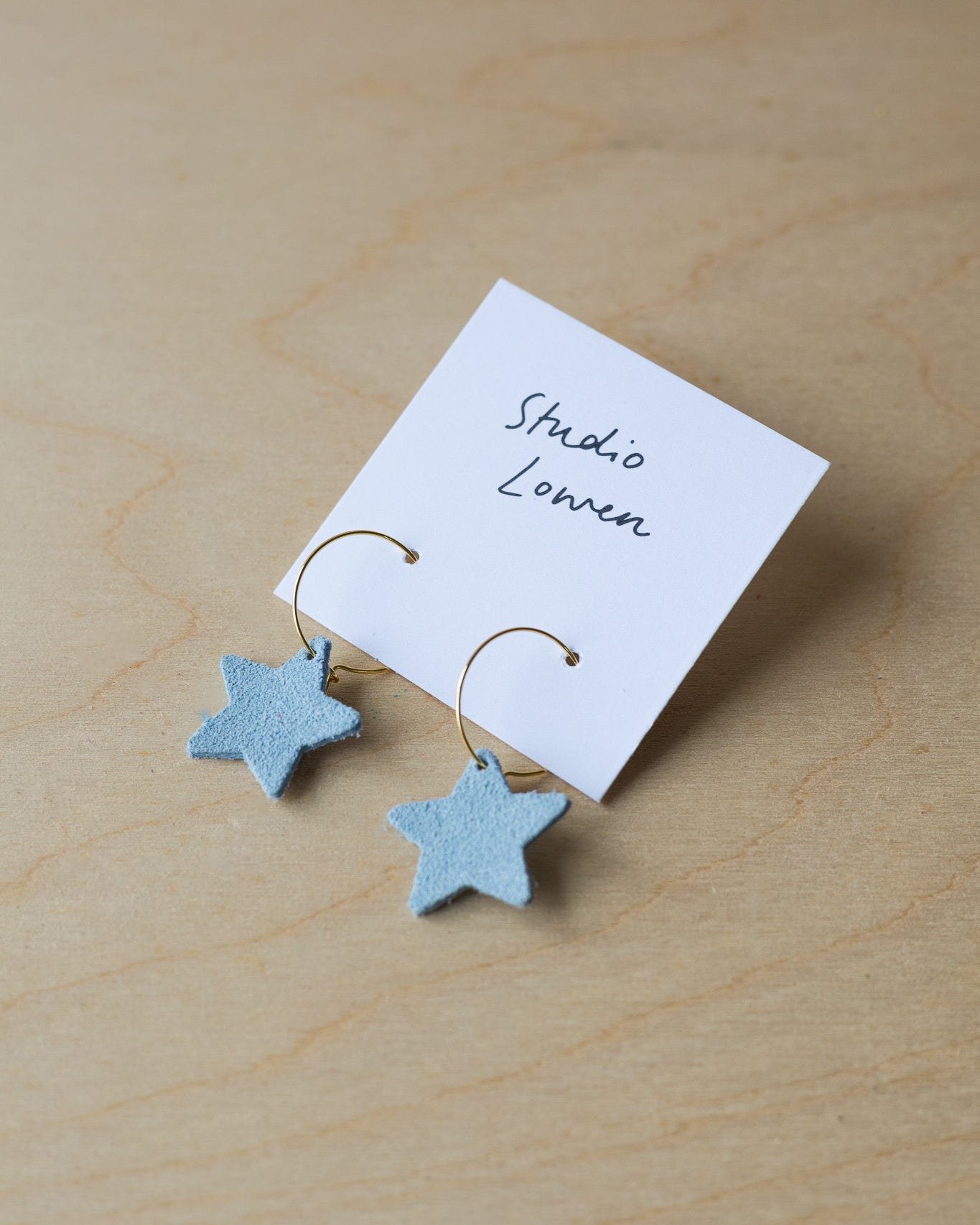 Star-shaped earrings on a card with 'Studio Lowen' branding on a wooden surface