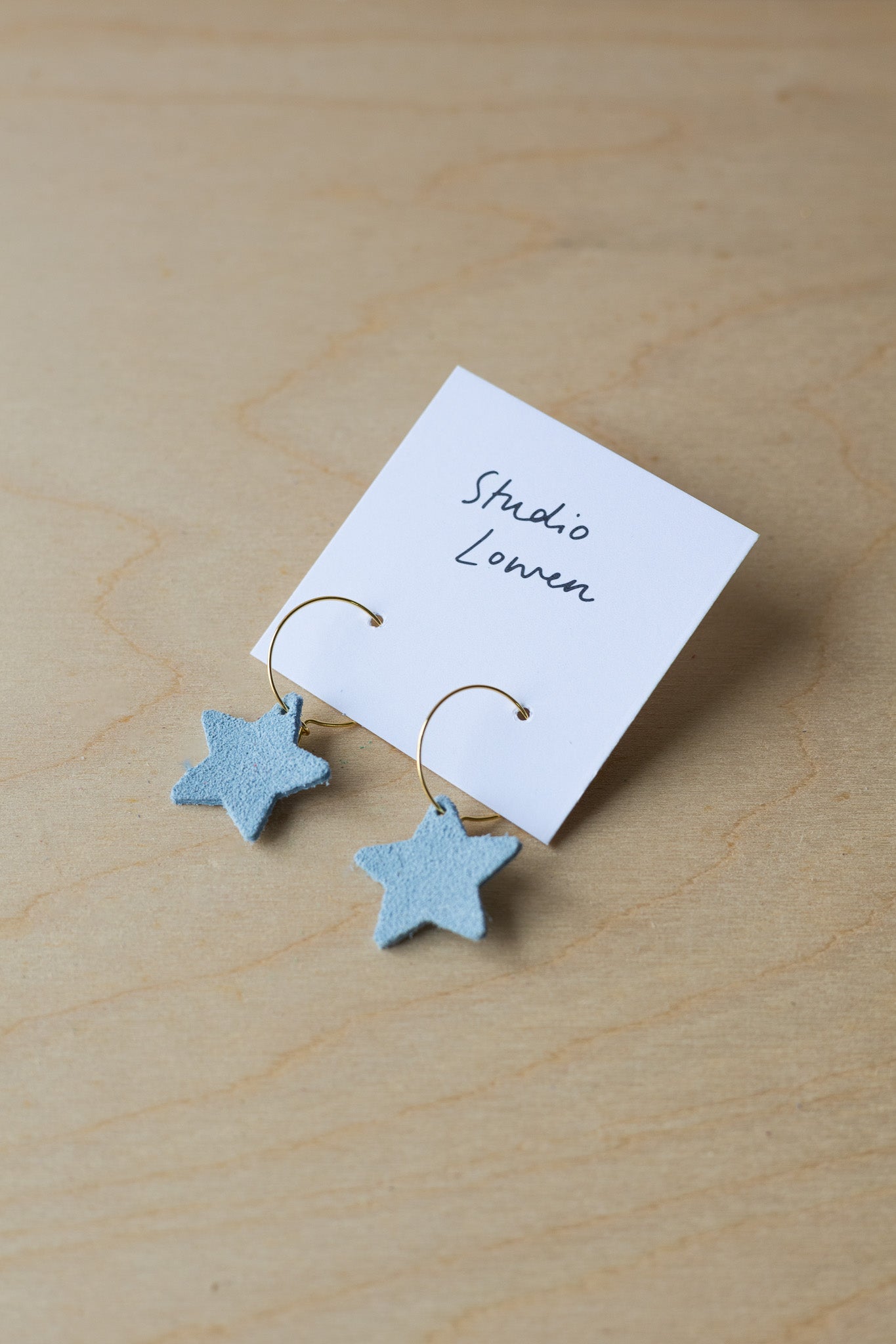 Star-shaped earrings on a card with 'Studio Lowen' branding on a wooden surface