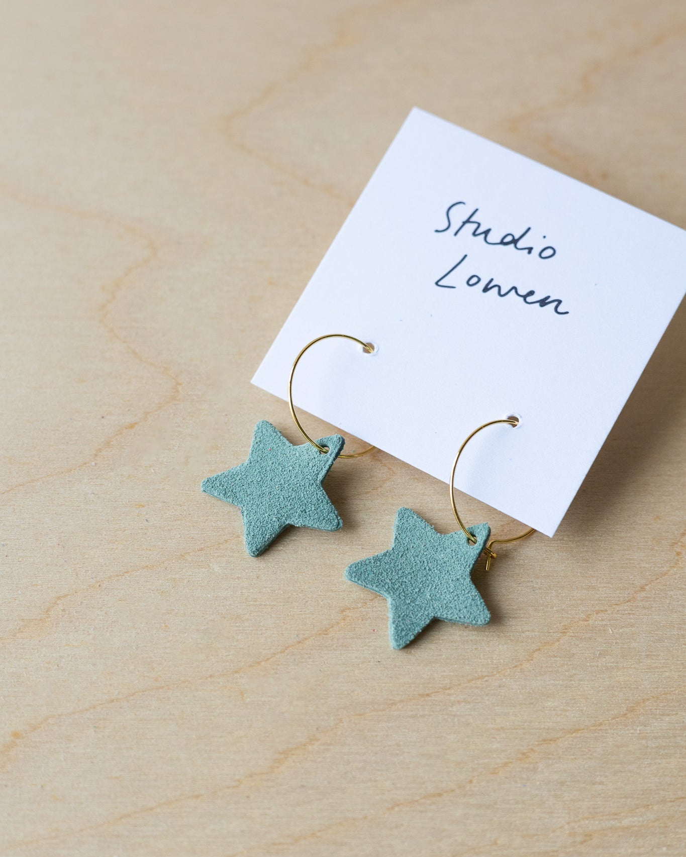 Mint green star-shaped earrings on a card with 'Studio Lowen' text on a wooden surface