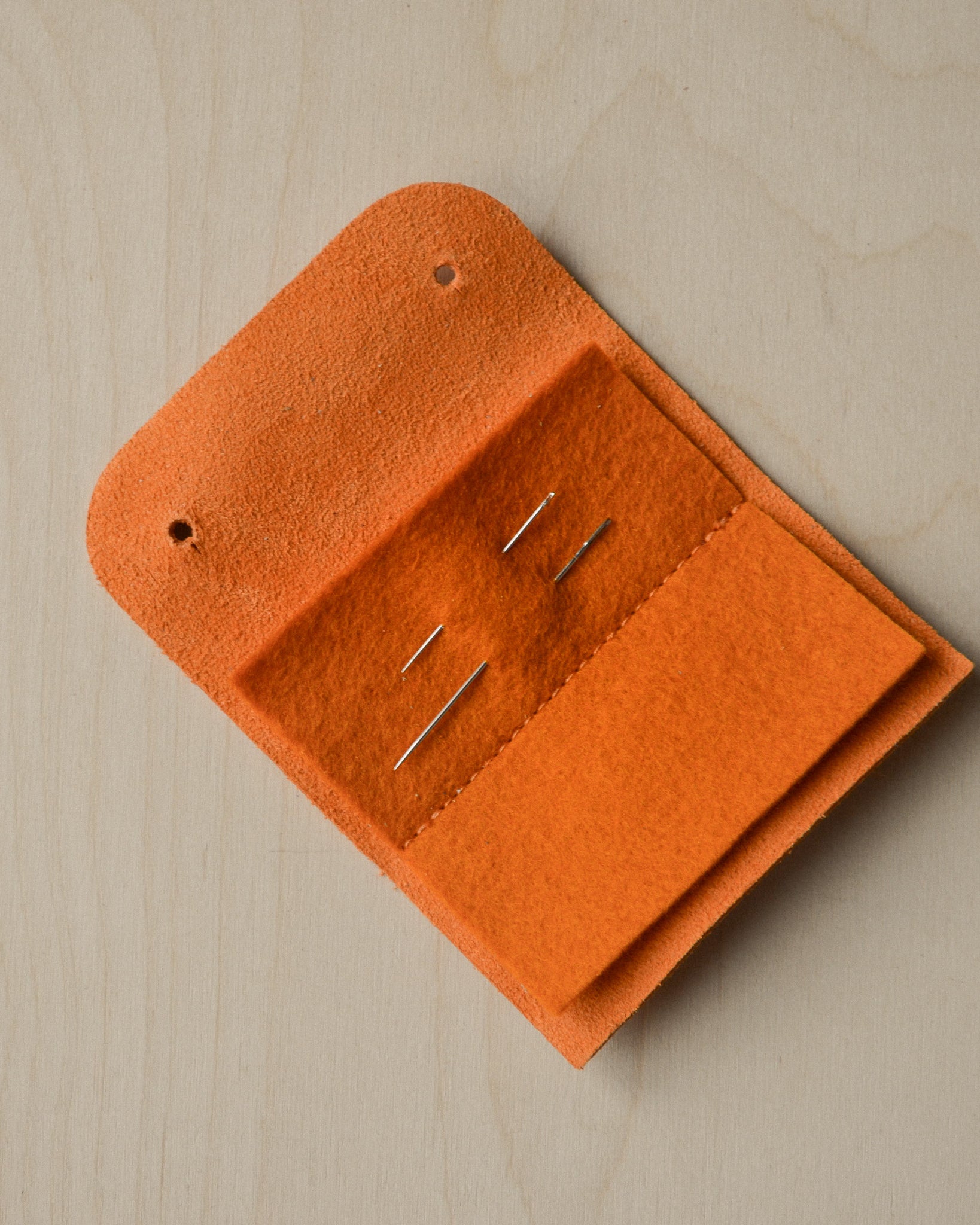Orange sewing needle case open with needles.