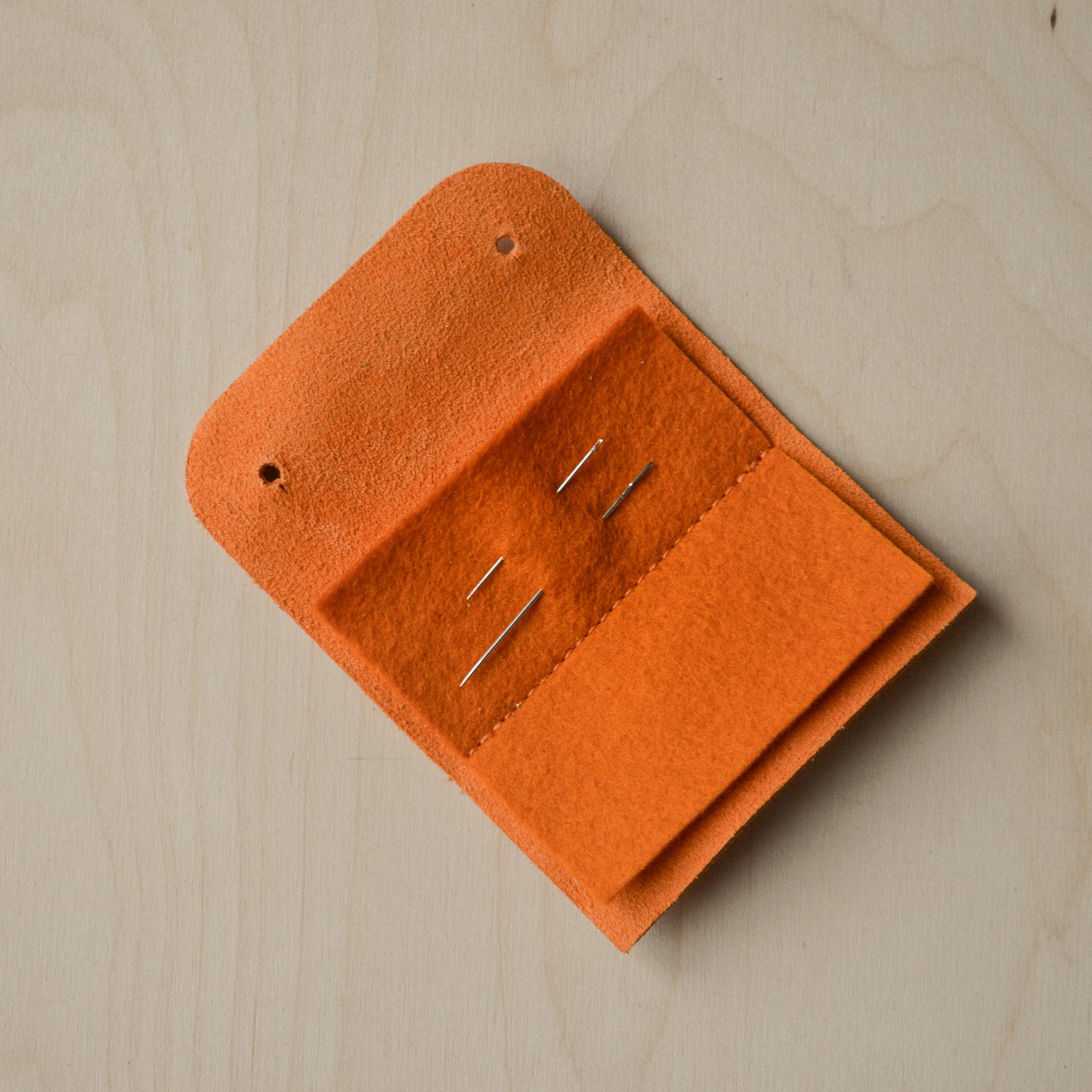 Orange sewing needle case open with needles.