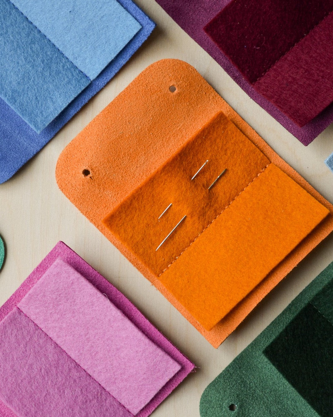 Suede sewing needle case in orange, cobalt blue, fuchsia pink and other colours.