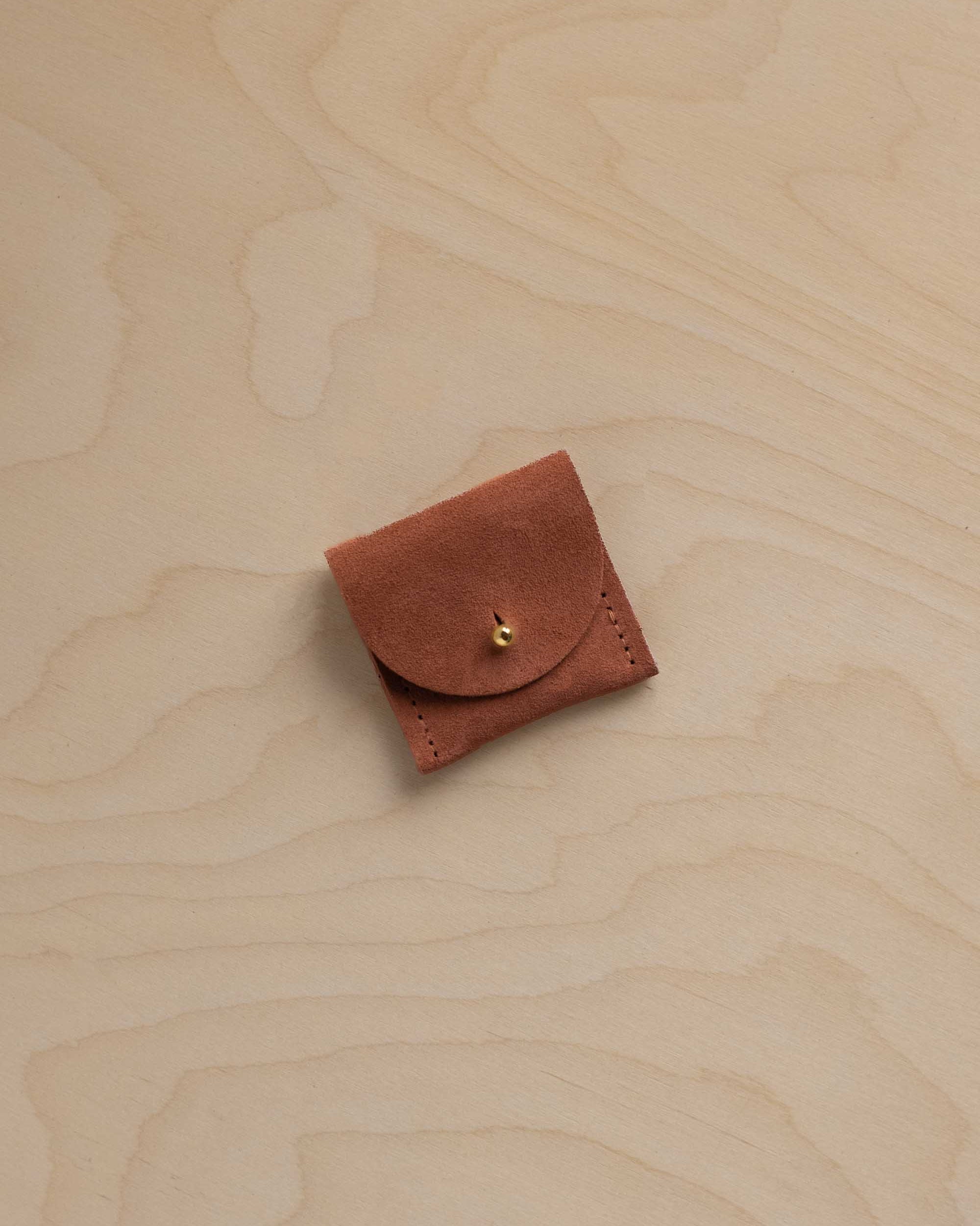 A small terracotta suede jewellery pouch on a wooden background.
