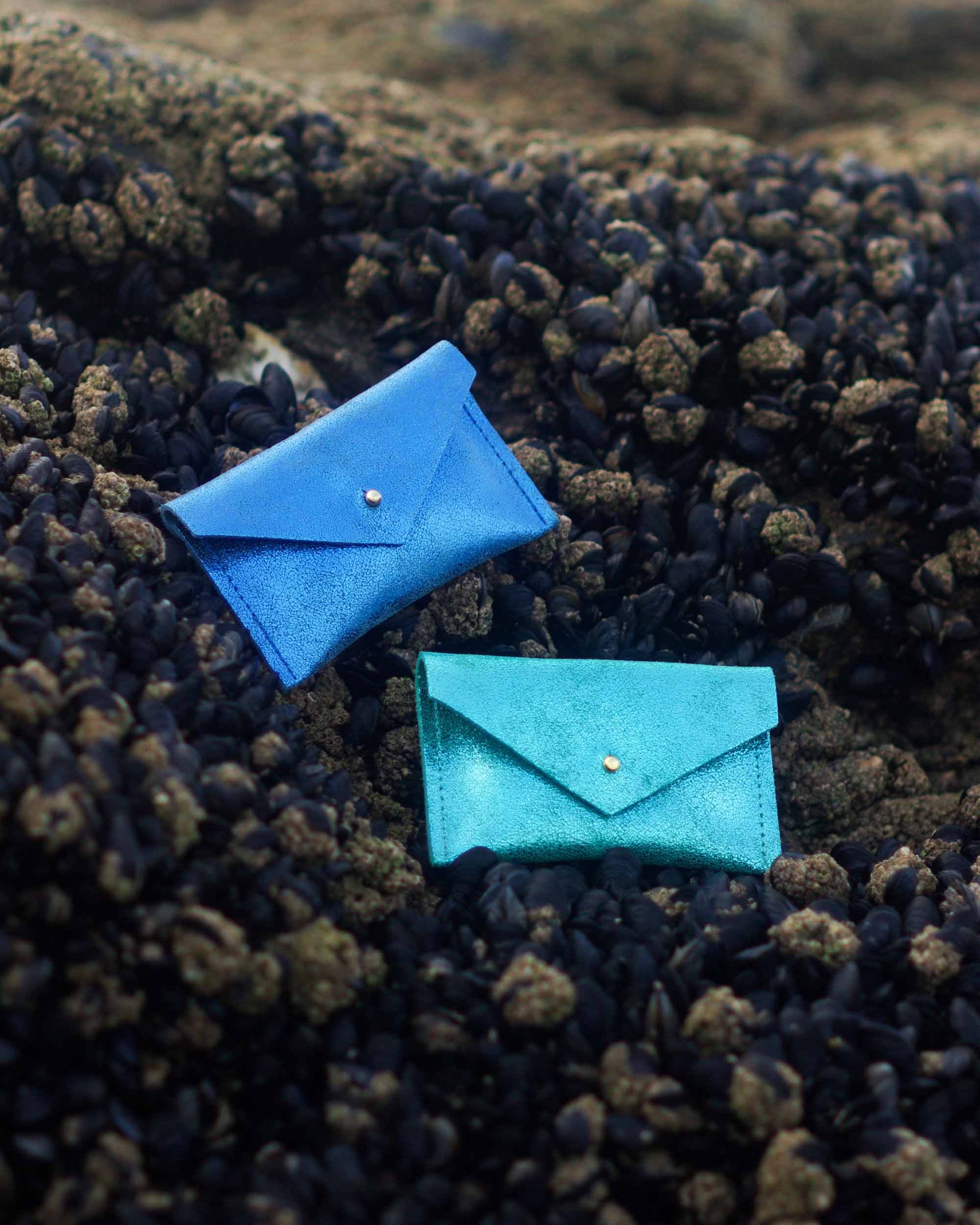 Two blue envelope leather wallets on a textured black surface