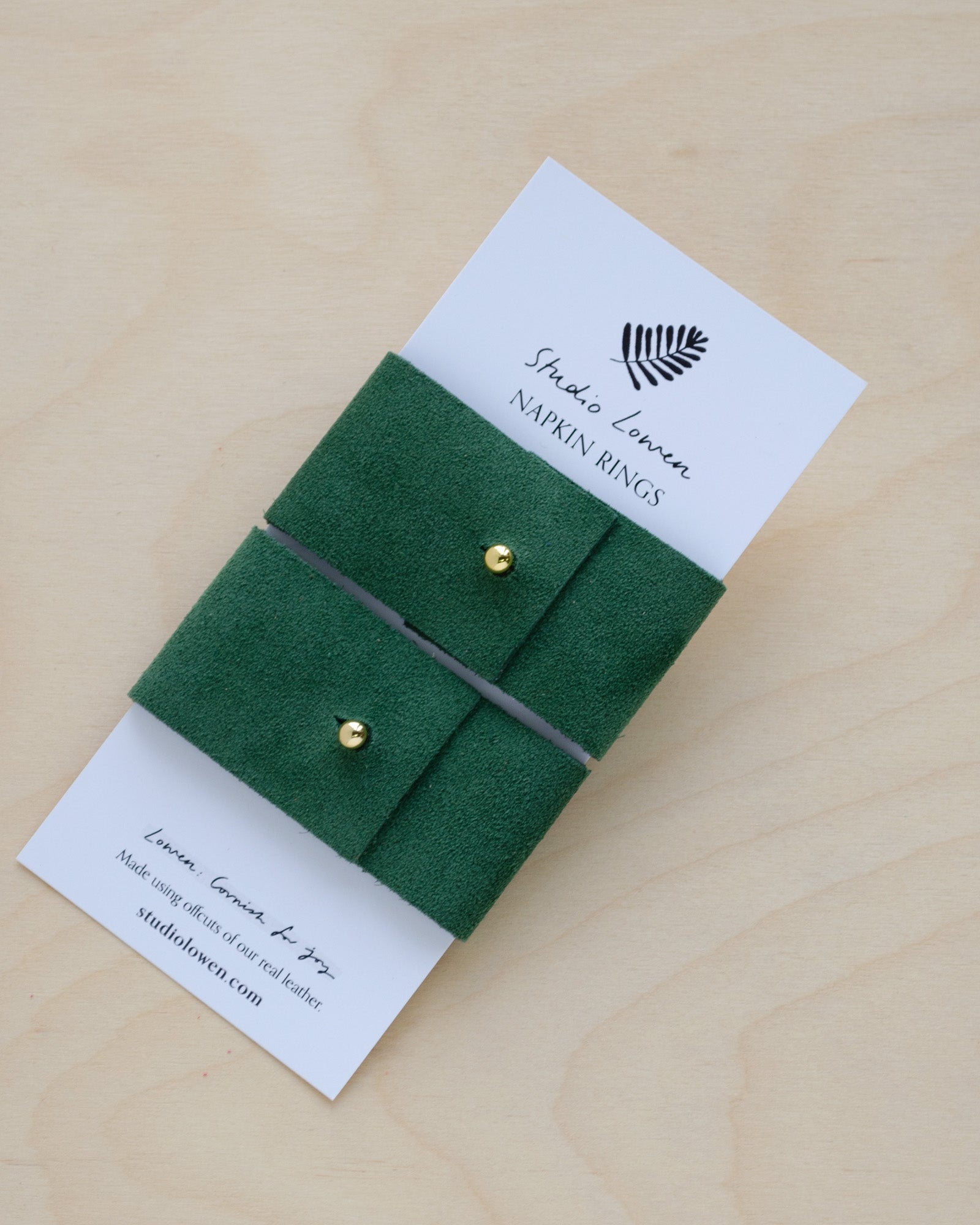 Pair of Moss Green suede napkin ring holders on a white card packaging.