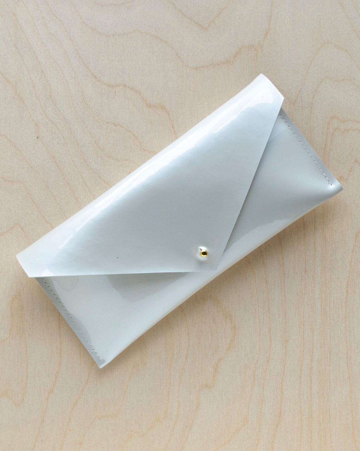 Envelope style compact clutch bag in a mother of pearl leather sits against a wooden background with gold hardware.