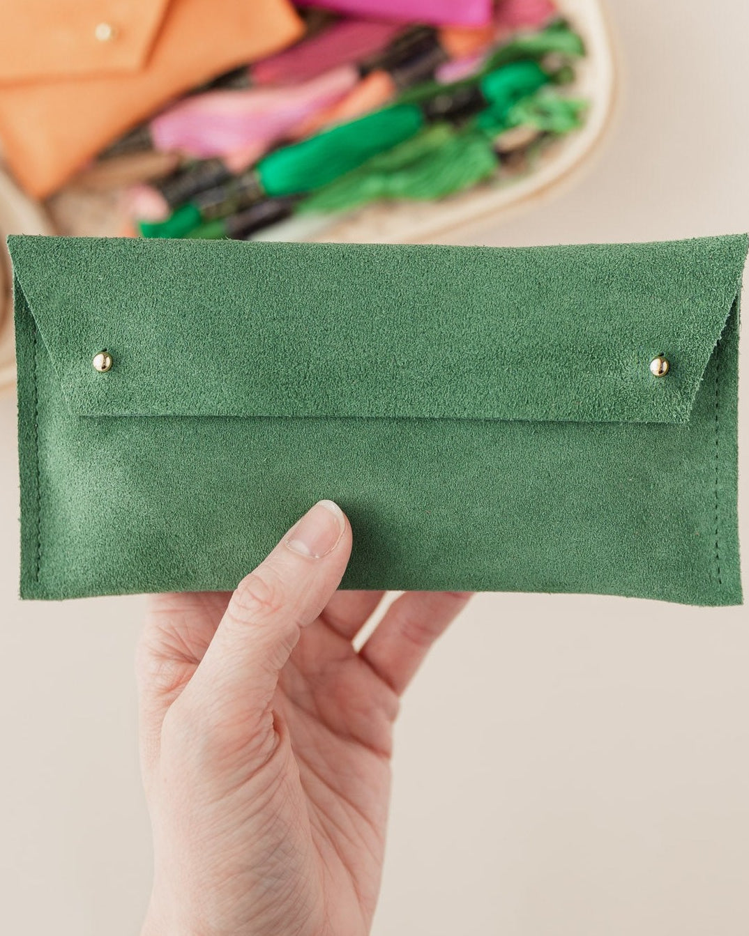 A suede notions pouch, in Moss Green by held up by hand.
