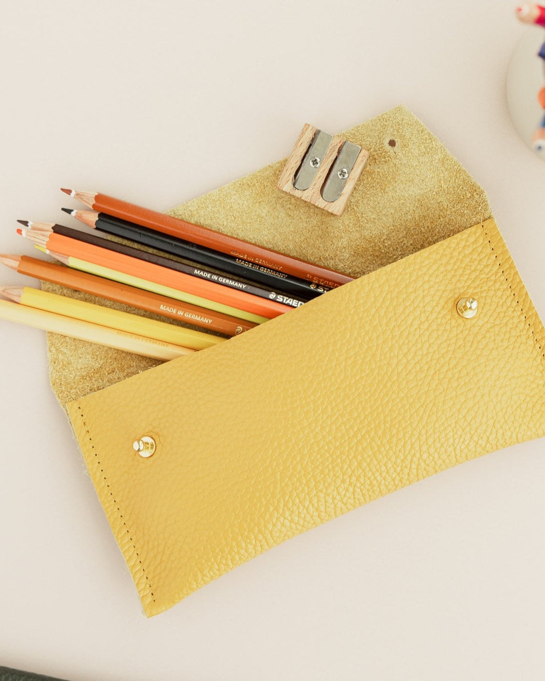 Open yellow leather pencil case with colourful pencils coming out and sharper.
