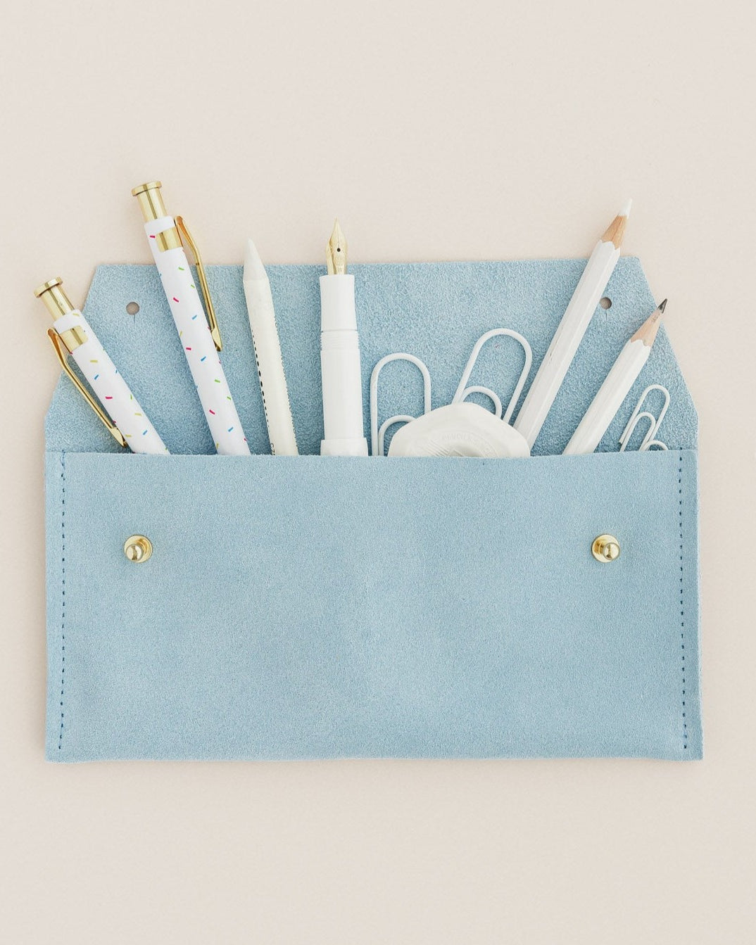 A suede pencil case in pale blue, featuring all the things you my find in a pencil case.