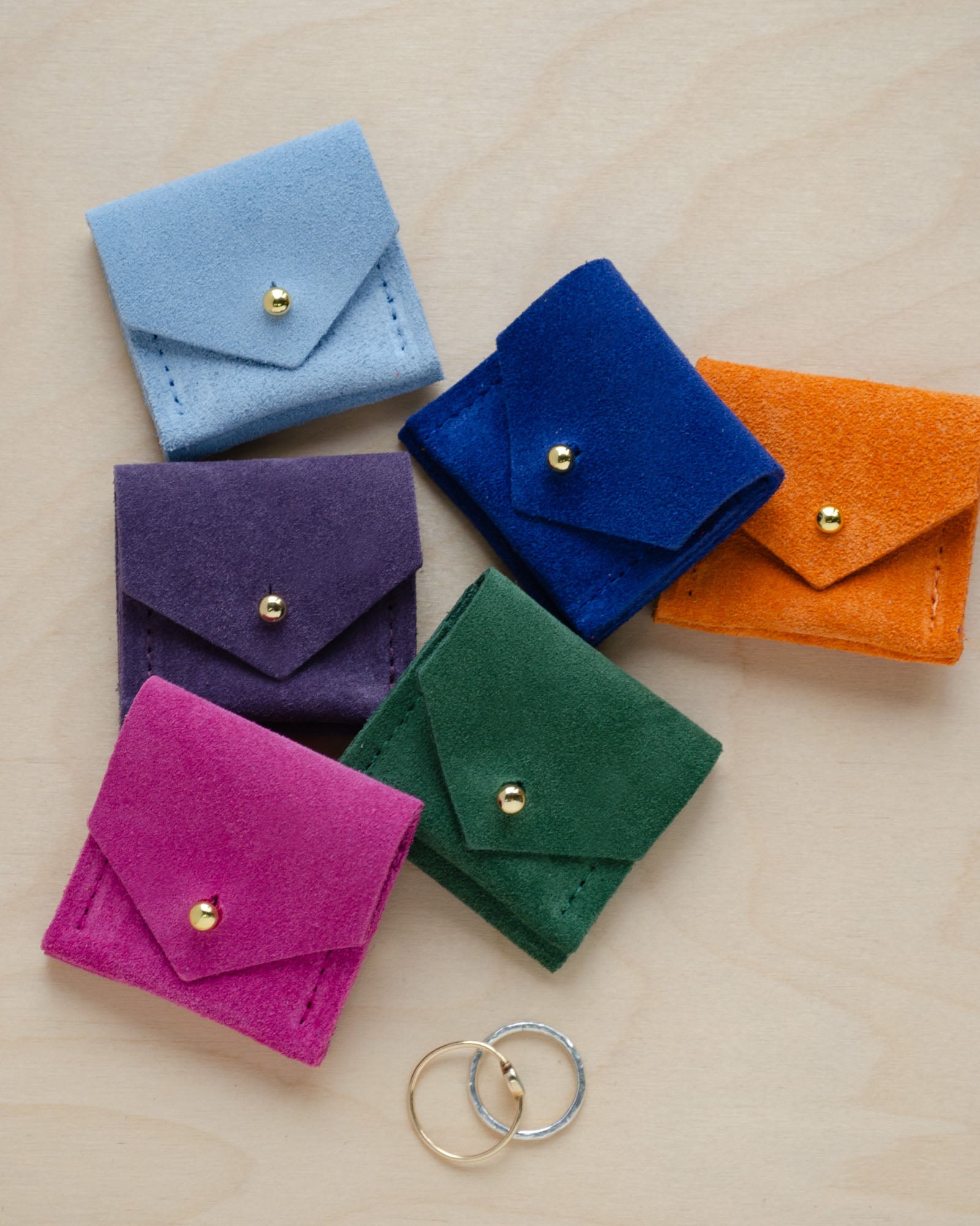 Six of the Wedding Ring Pouches in suede. Colours are, Pale Blue, Grape Purple, Ultramarine Blue, Clementine Orange, Fuchsia Pink and Moss Green