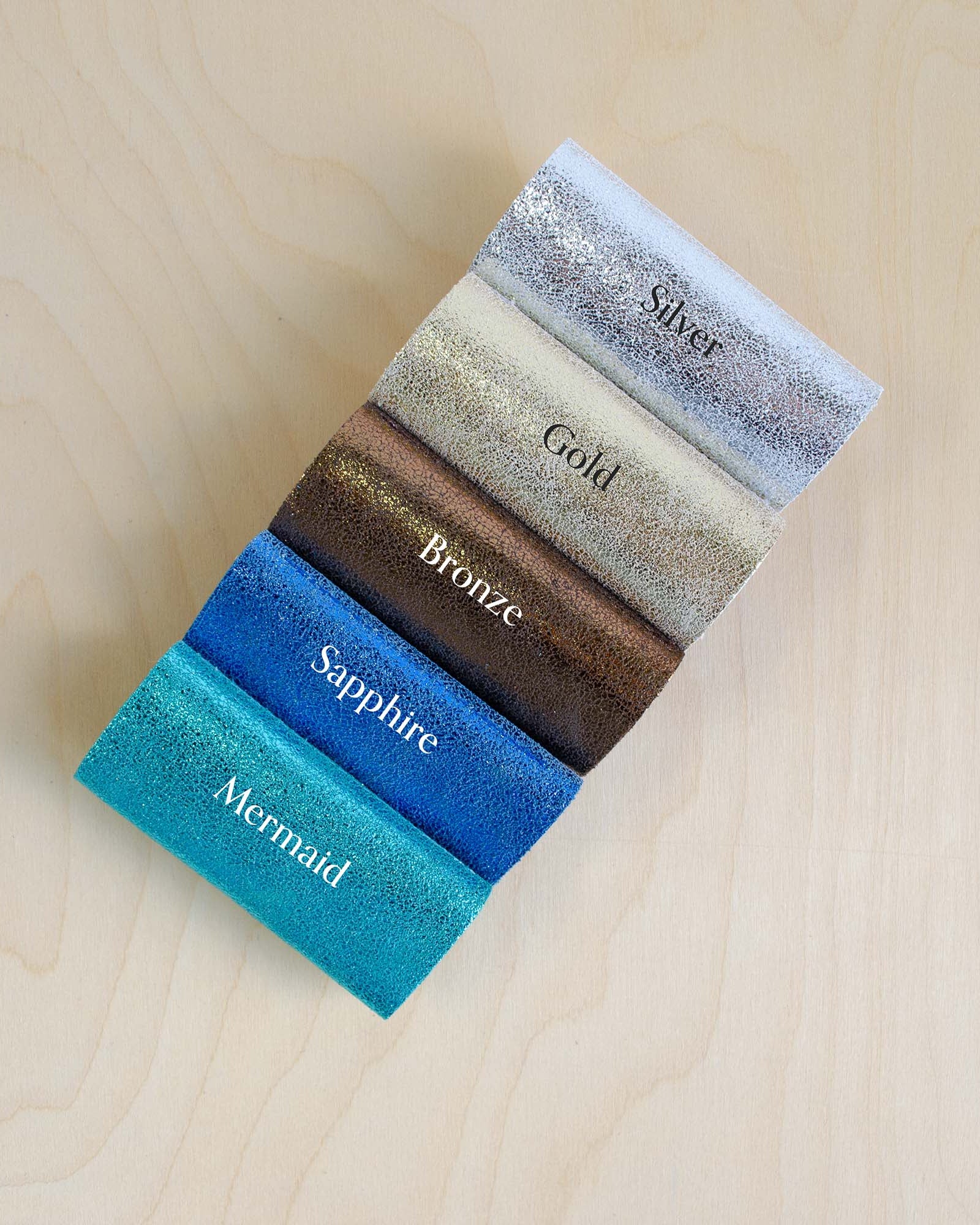 Color swatch samples labeled 'Silver', 'Gold', 'Bronze', 'Sapphire', and 'Mermaid' on a wooden surface.