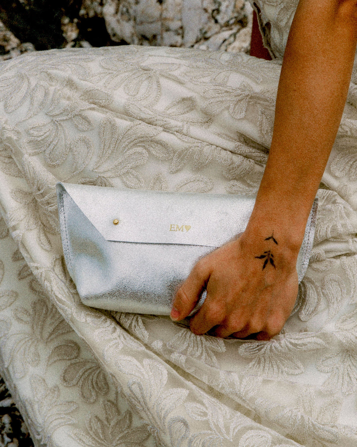 Bride holds a metallic silver clutch bag against her wedding dress.