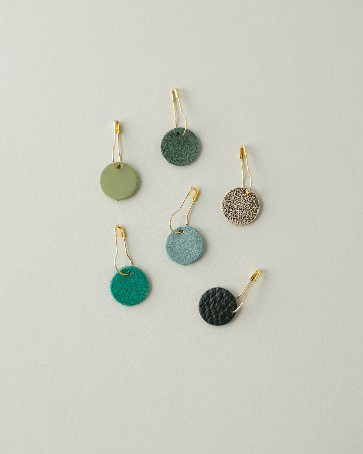 Colourful leather and suede stitch markers for knitting in greens and gold.