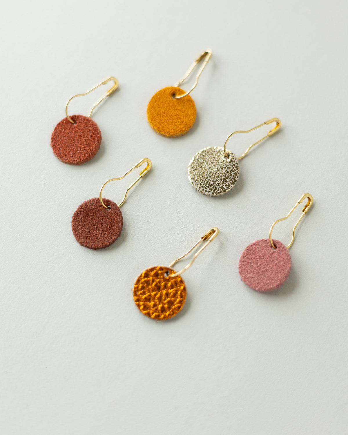 Colourful leather and suede stitch markers for knitting in oranges and browns.