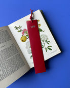 Red bookmark with a heart design on an open book with botanical illustrations against a blue background