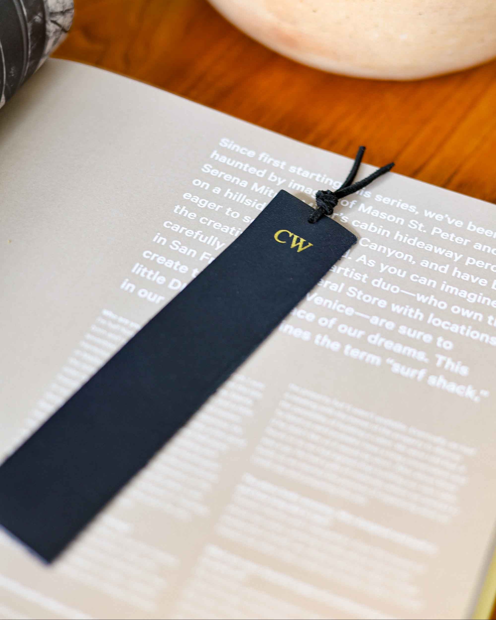 Navy blue bookmark with 'CW' initials on a book with a blurred background