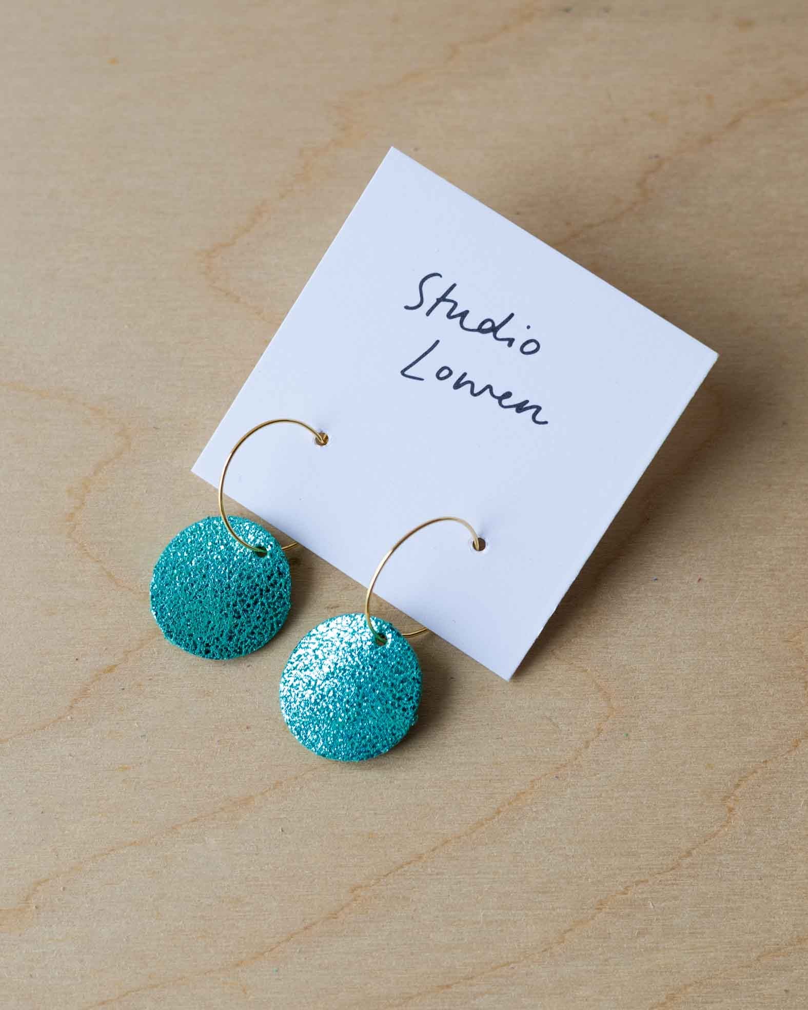 Turquoise leather earrings on a card with 'Studio Lowen' branding on a wooden surface