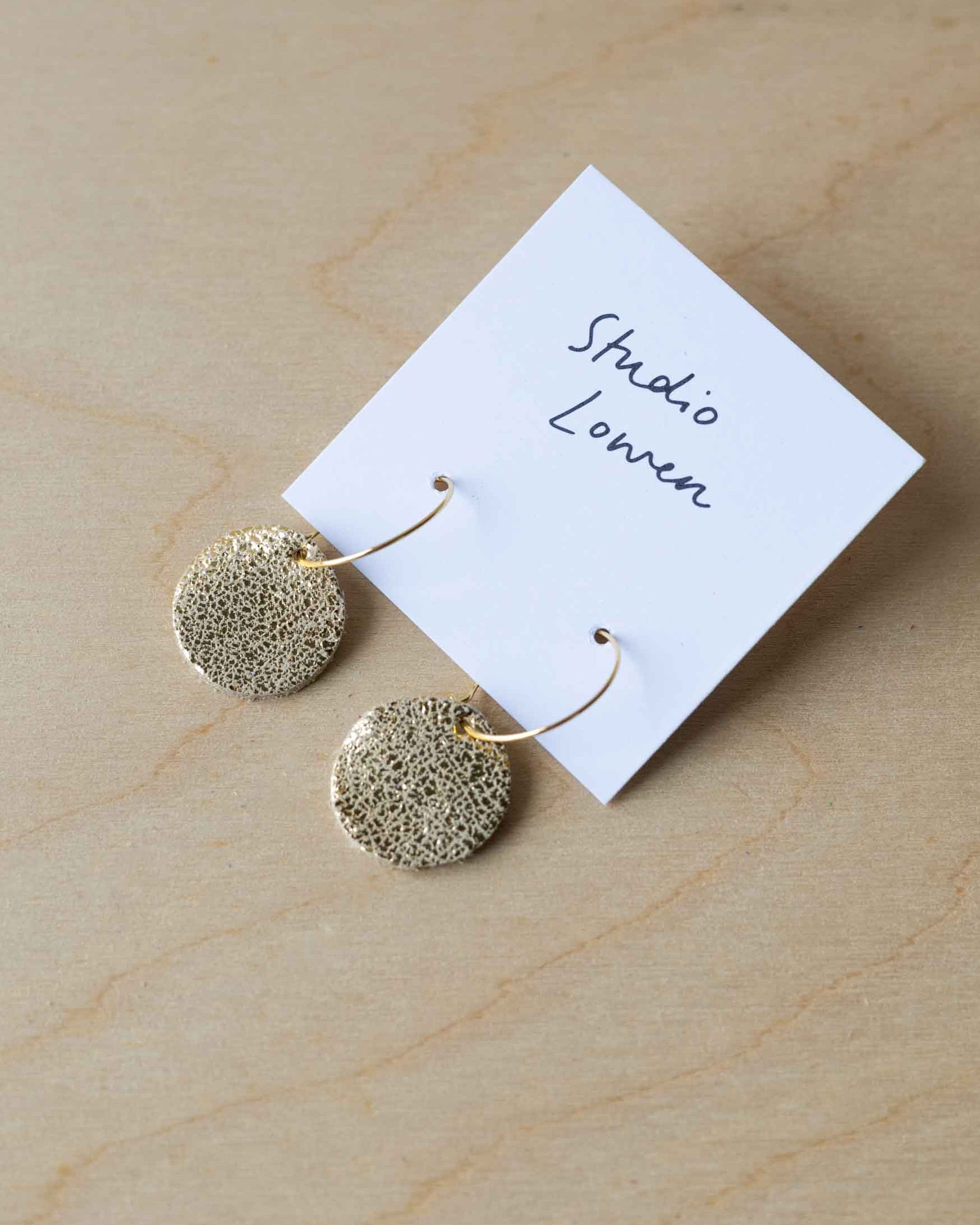 Gold round earrings on a 'Studio Lowen' branded card on a wooden surface