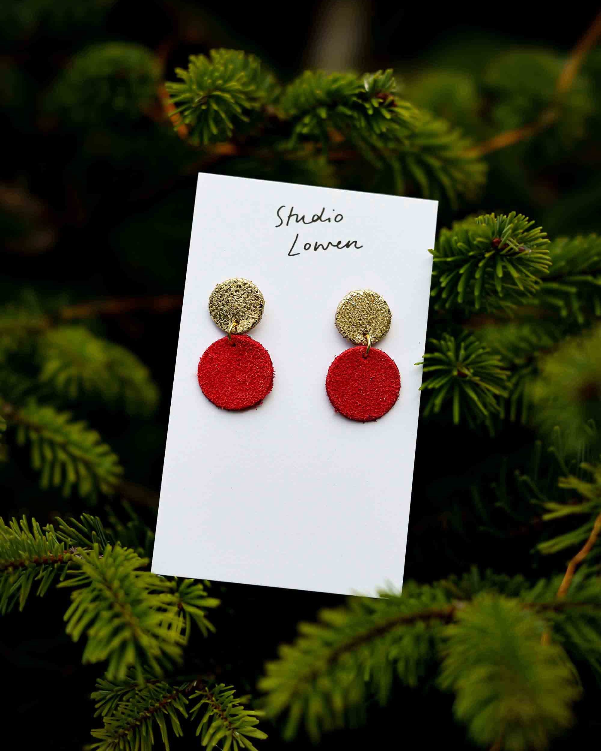 Red and gold leather earrings on a card with 'Studio Lowen' text, set against a green foliage background.