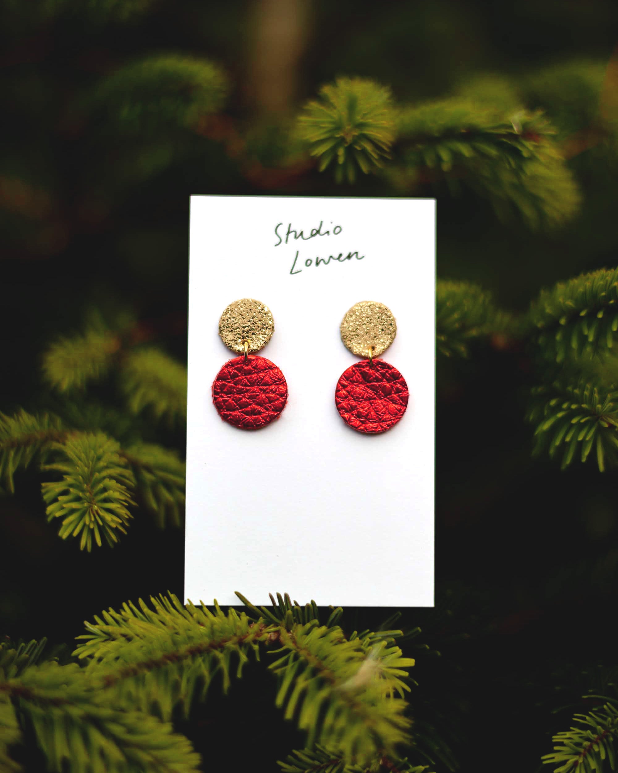 Red and gold earrings on a card with a green leafy Christmas tree background