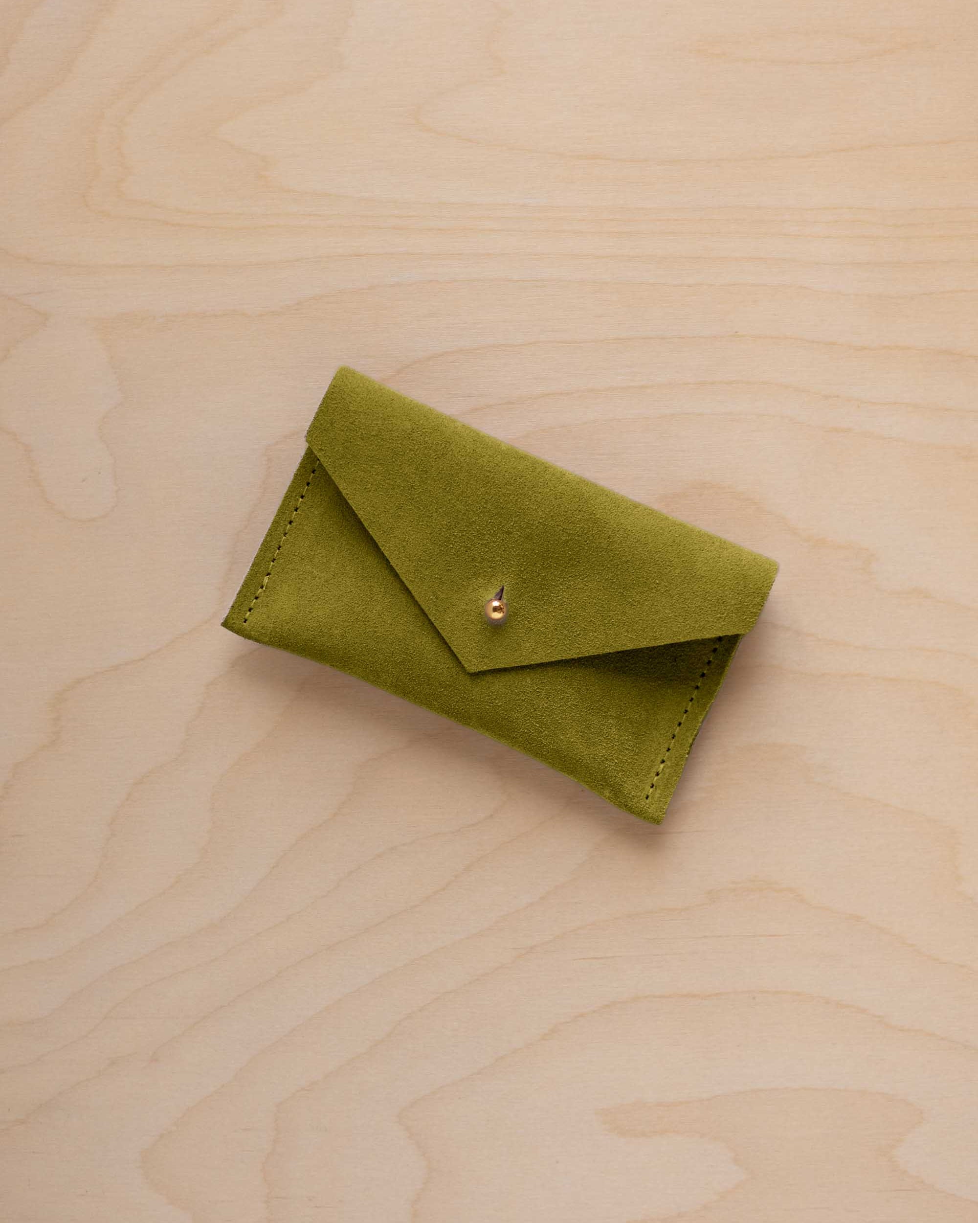 A small chartreuse green coloured suede pouch with a flap closure and gold coloured fastening, on a light wood grain surface.