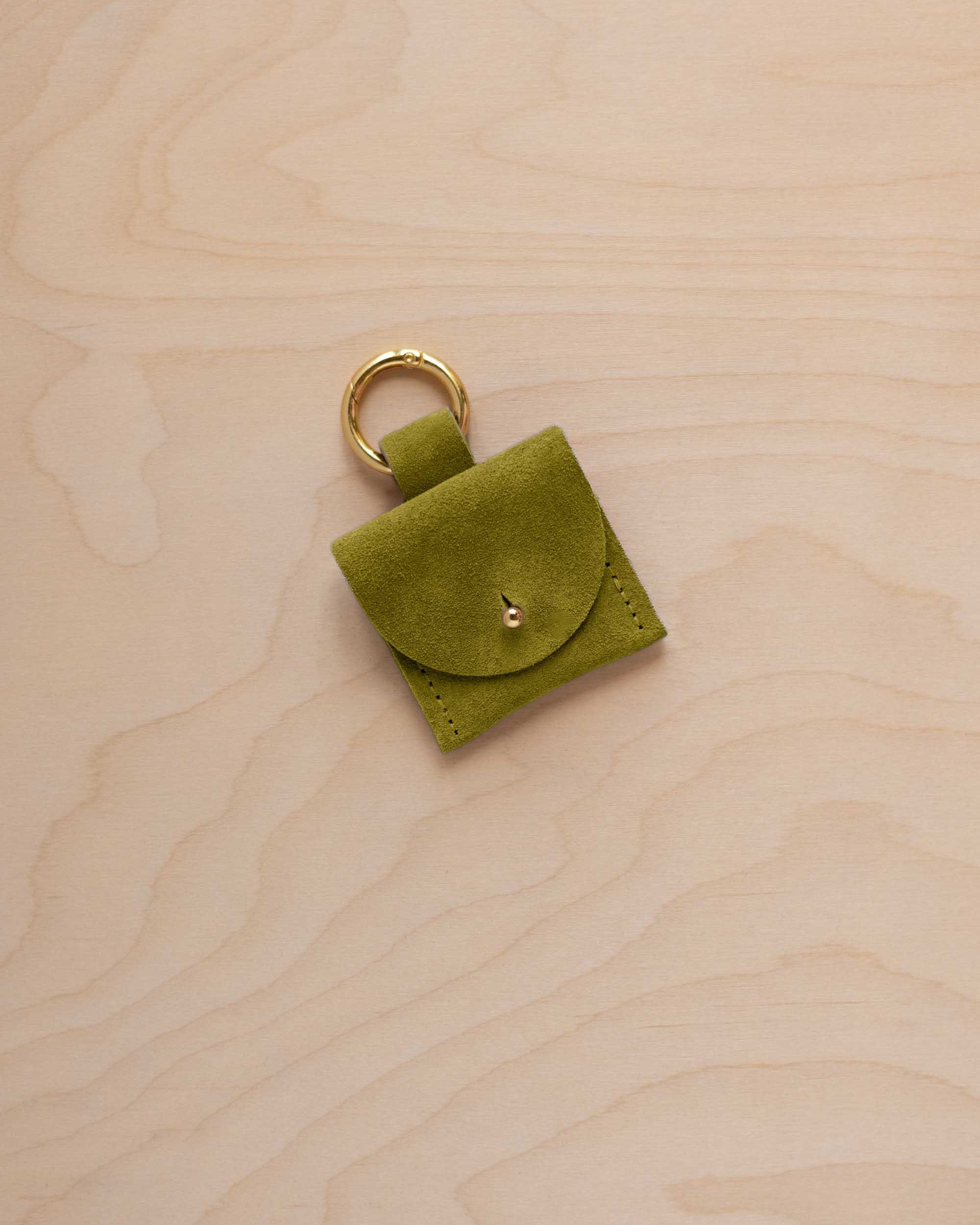 A small chartreuse lime green coloured suede pouch bag charm with a gold coloured clip ring fastening, displayed on a light wood grain background.