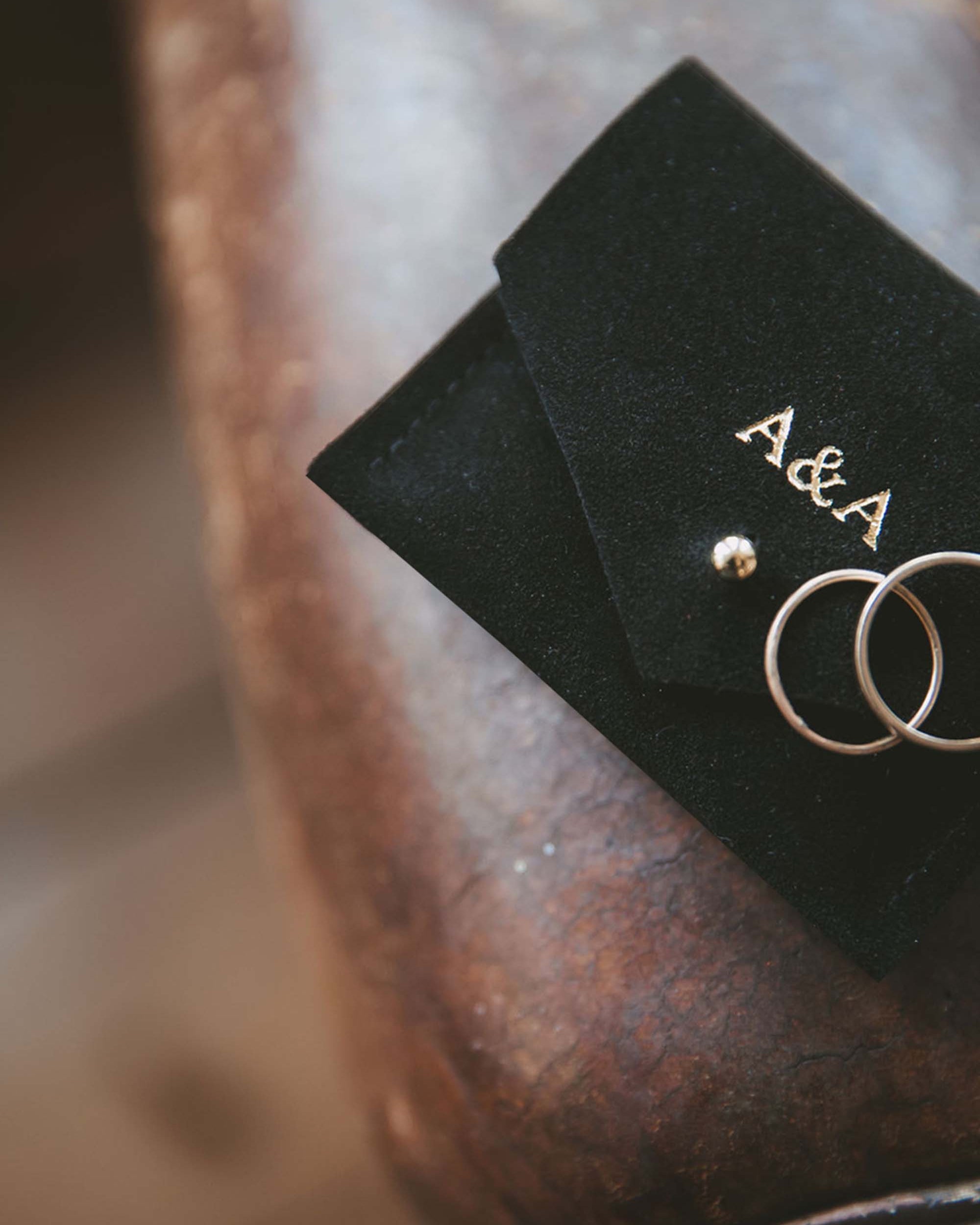Small black suede jewellery pouch with gold foiled couples initials on the front with two gold wedding rings.