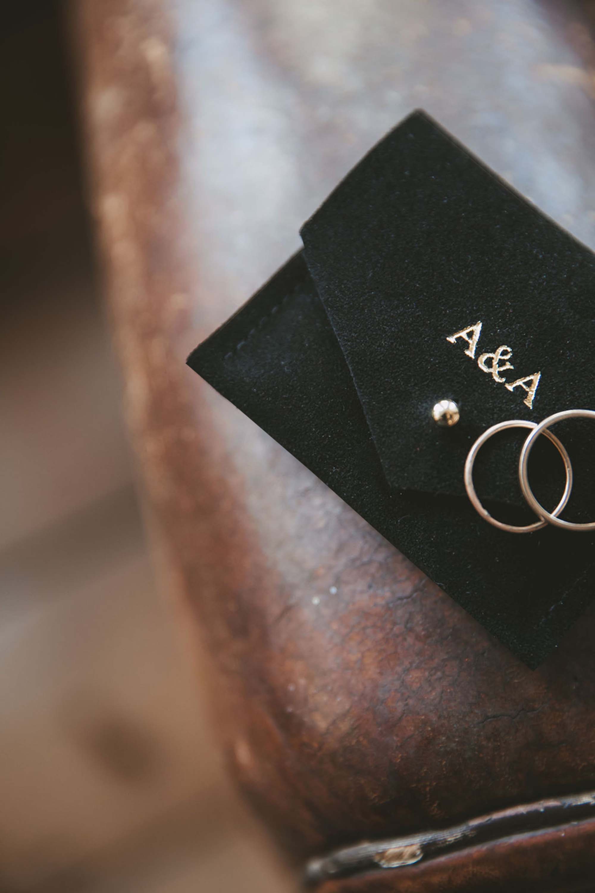 Small black suede jewellery pouch with gold foiled couples initials on the front with two gold wedding rings.