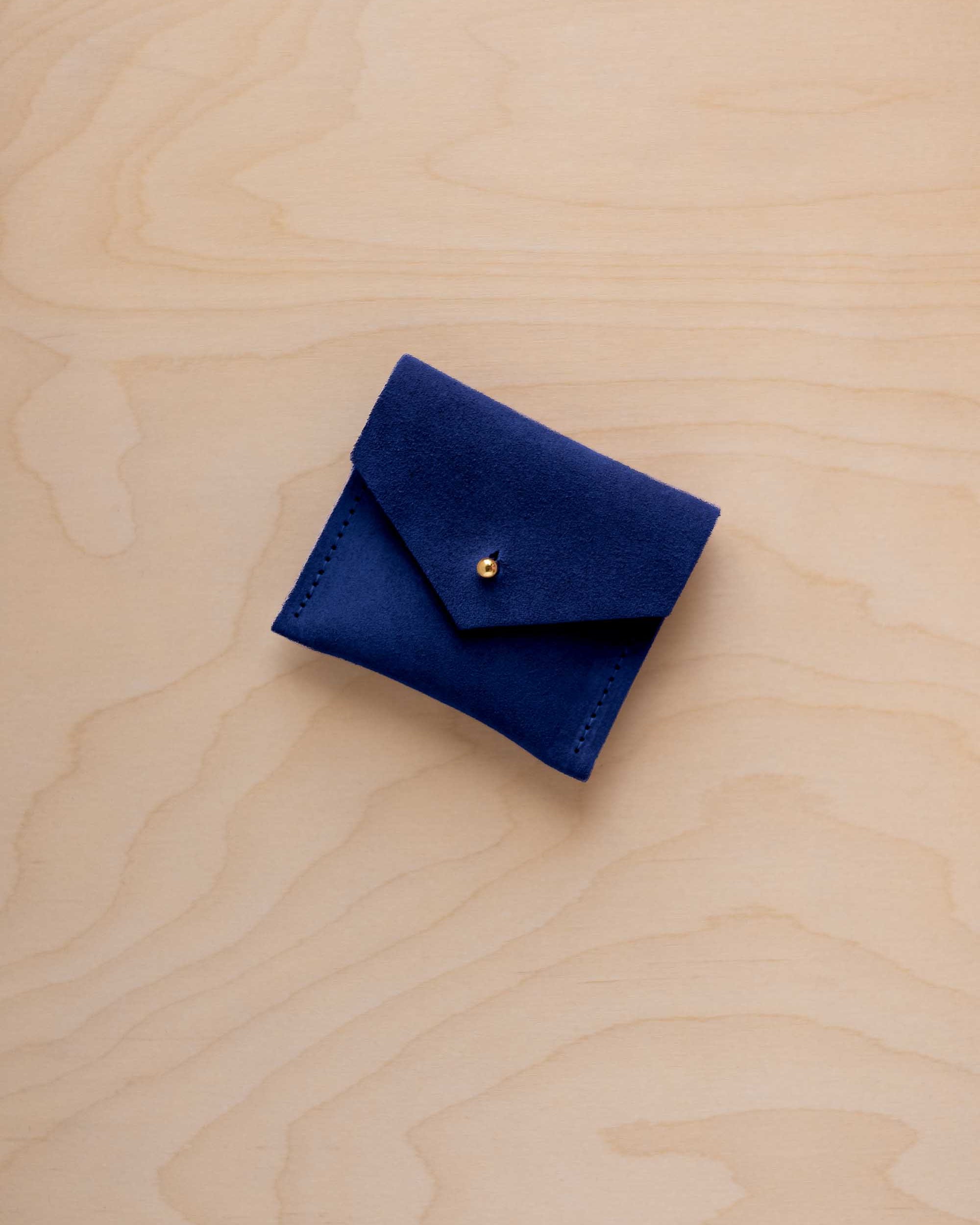 A small dark royal blue felt pouch with a flap closure and a gold button, placed on a light wood grain surface.