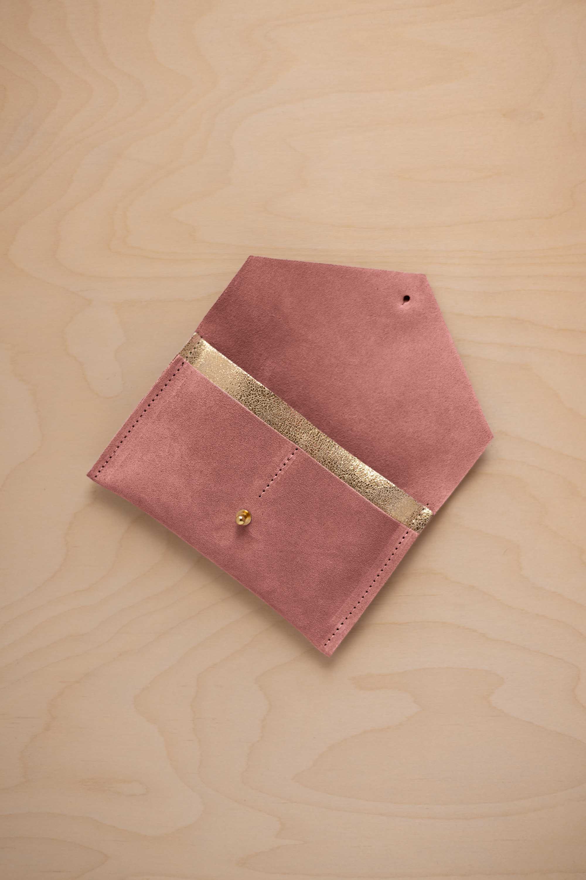 A dusty rose pink coloured suede pouch with a metallic gold contrast pocket and a small gold stud, displayed on a light wood grain background.