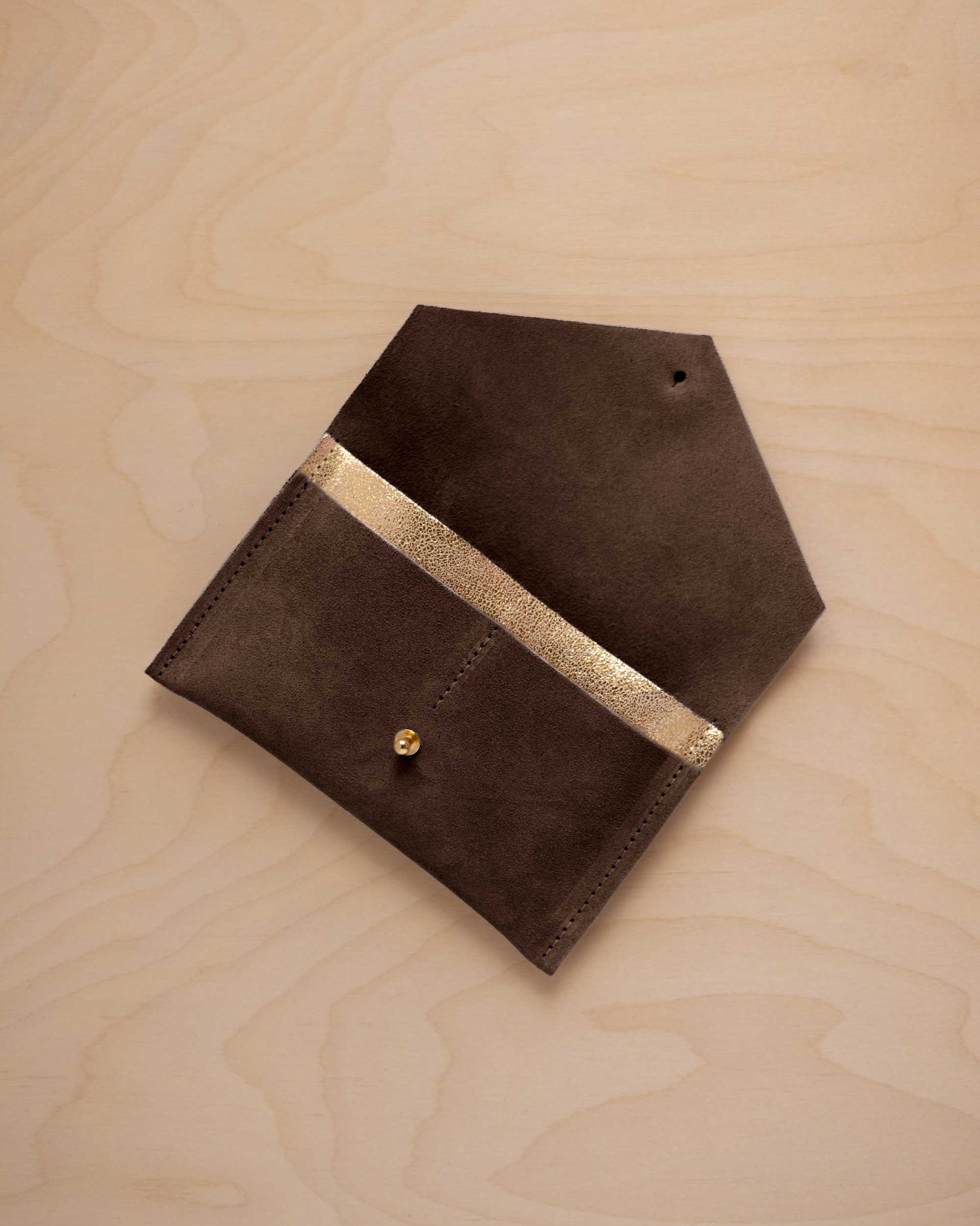 An espresso brown coloured suede pouch with a metallic gold contrast pocket and a small gold stud, displayed on a light wood grain background.