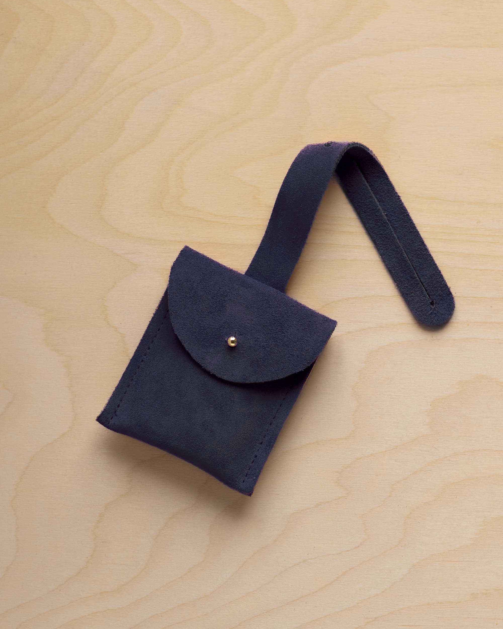 A small midnight navy blue suede pouch with a flap closure and a matching strap, resting on a light wood grain surface.